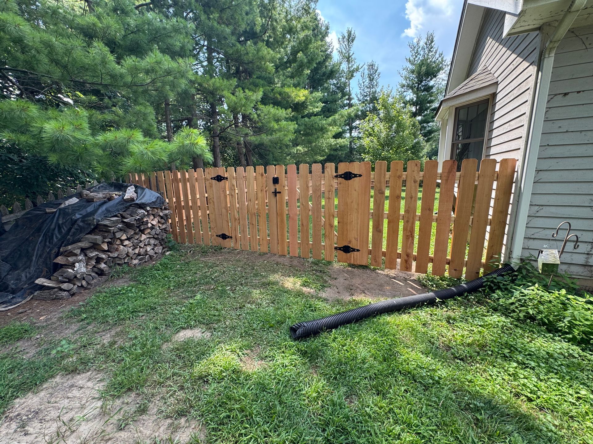 Wooden fence in yard next to a house with trees in the background.