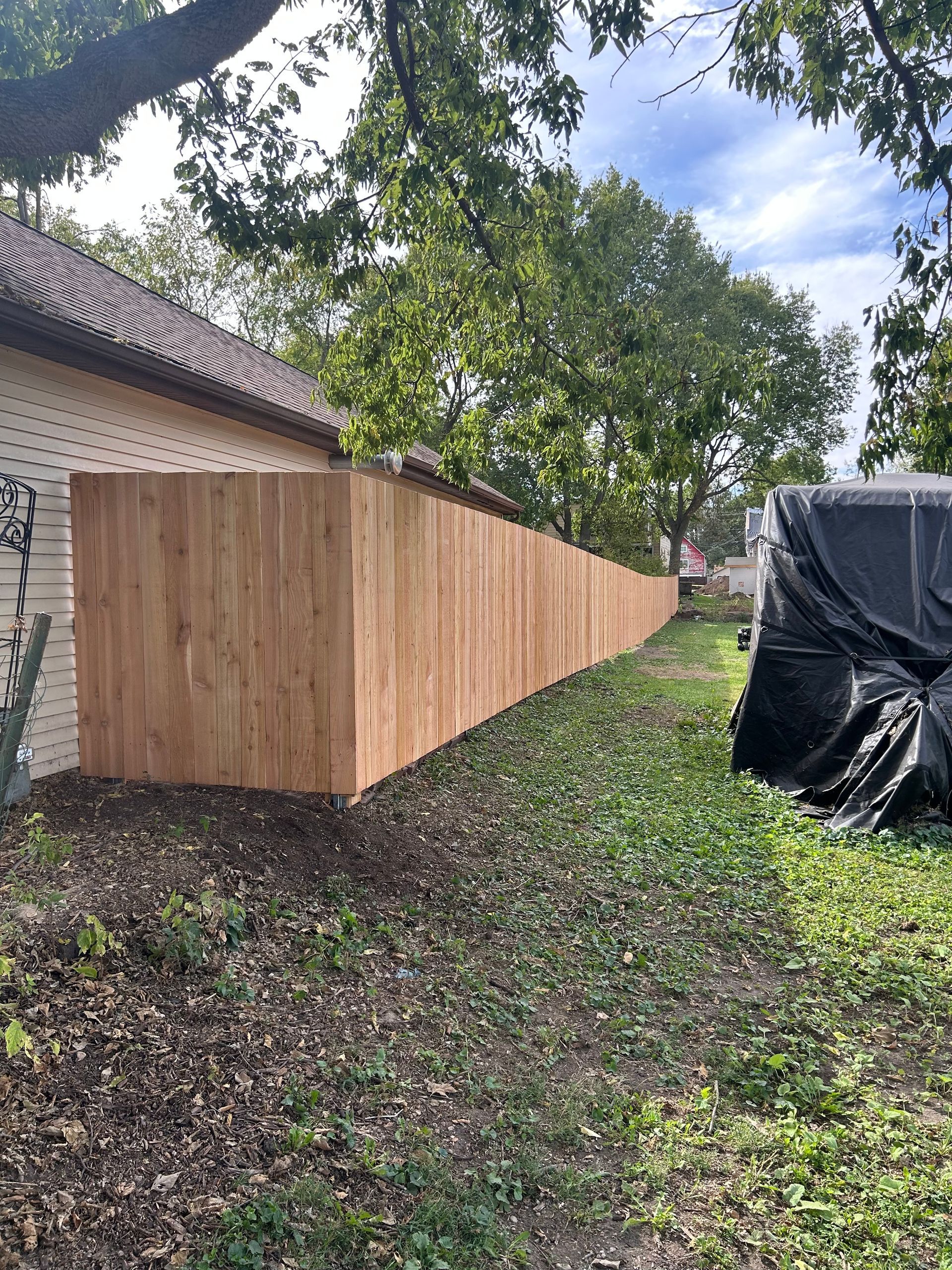 A long, wooden fence along the side of a building and a yard with green grass, under a cloudy sky.