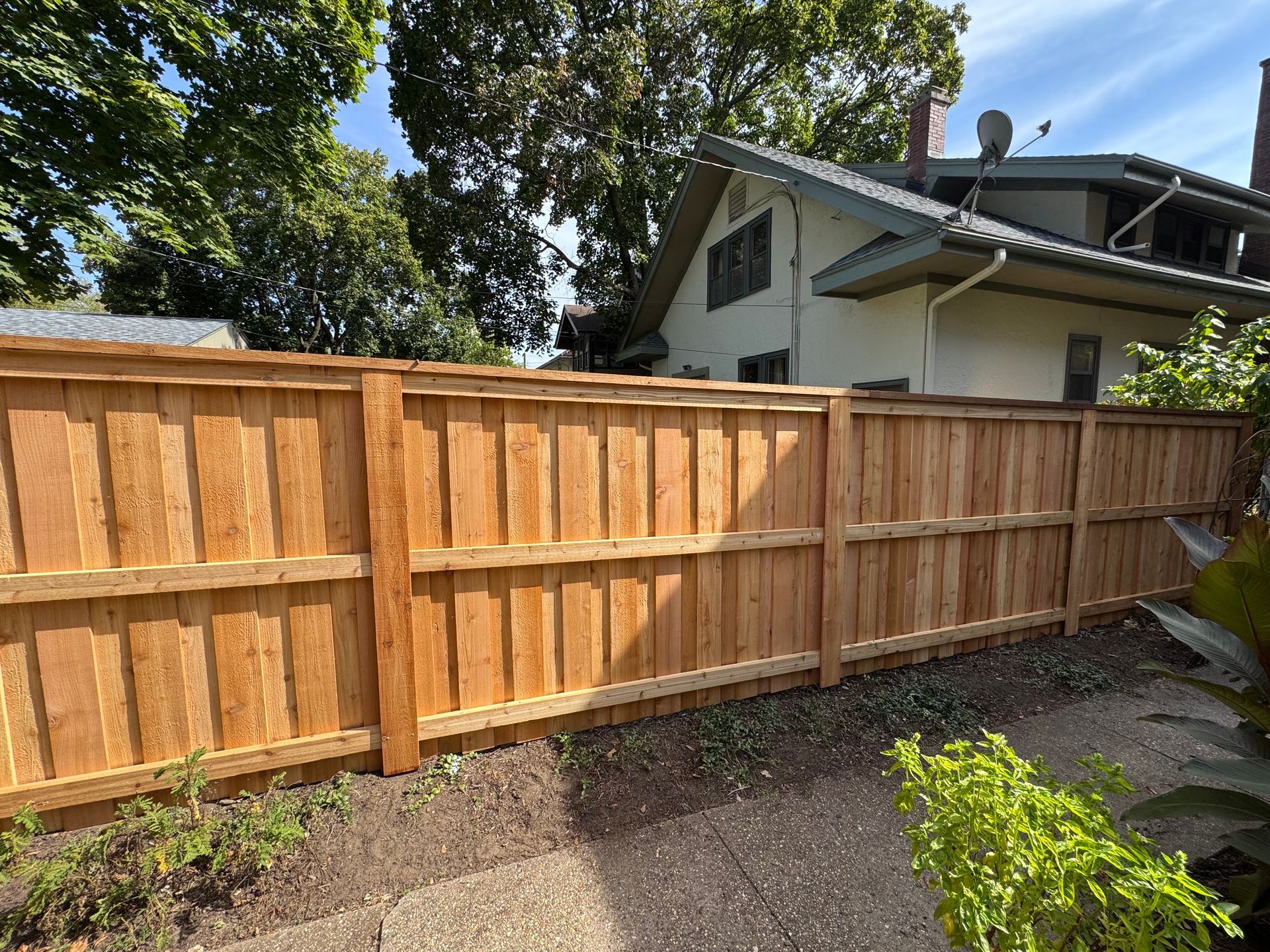 Wooden fence in a backyard, with a house visible in the background under a blue sky.