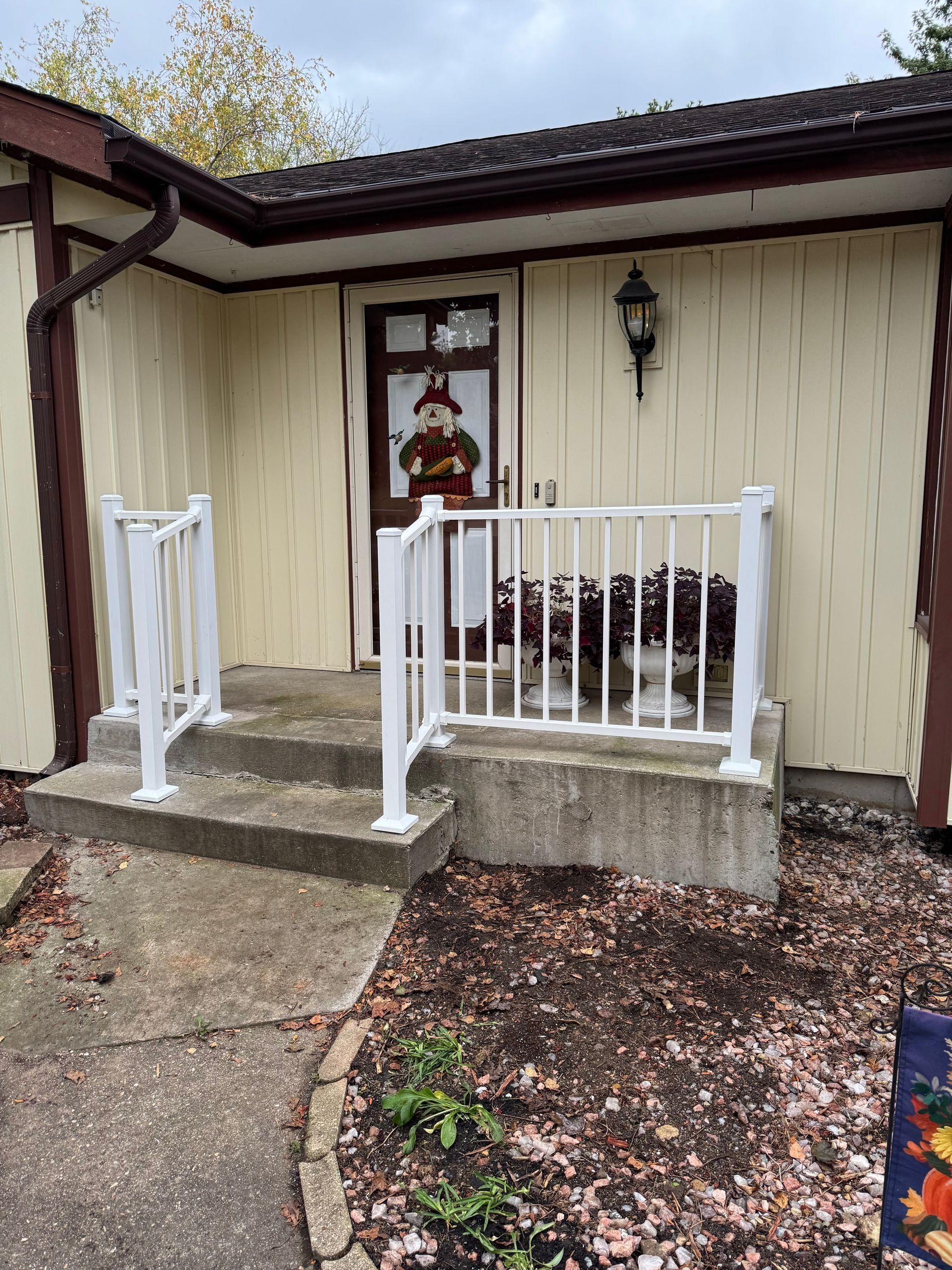 Front entrance with white railing, steps, and door decorated with a Santa. Light beige siding and brown trim.
