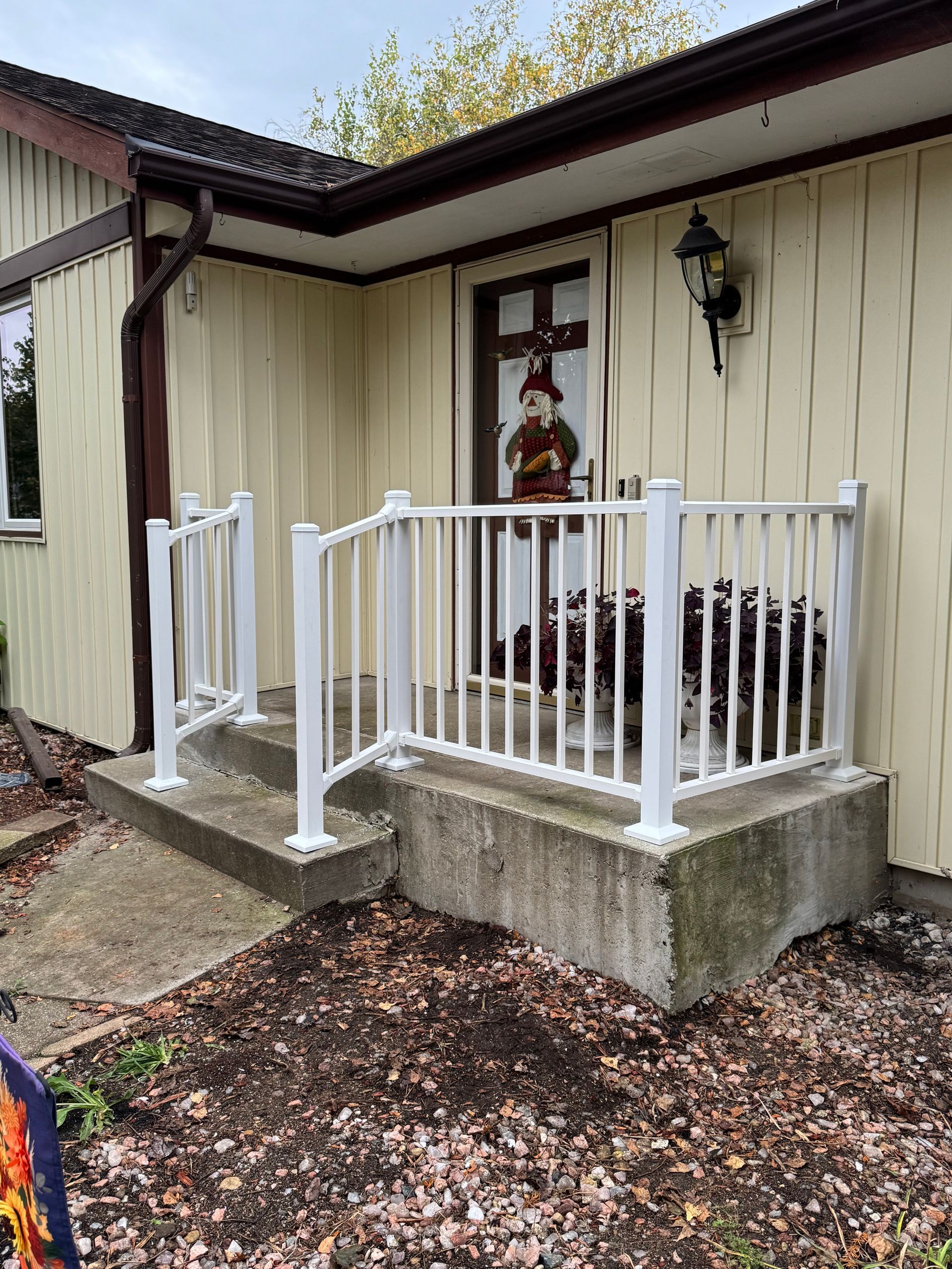 White railing on a concrete porch leading to a front door of a light yellow house.