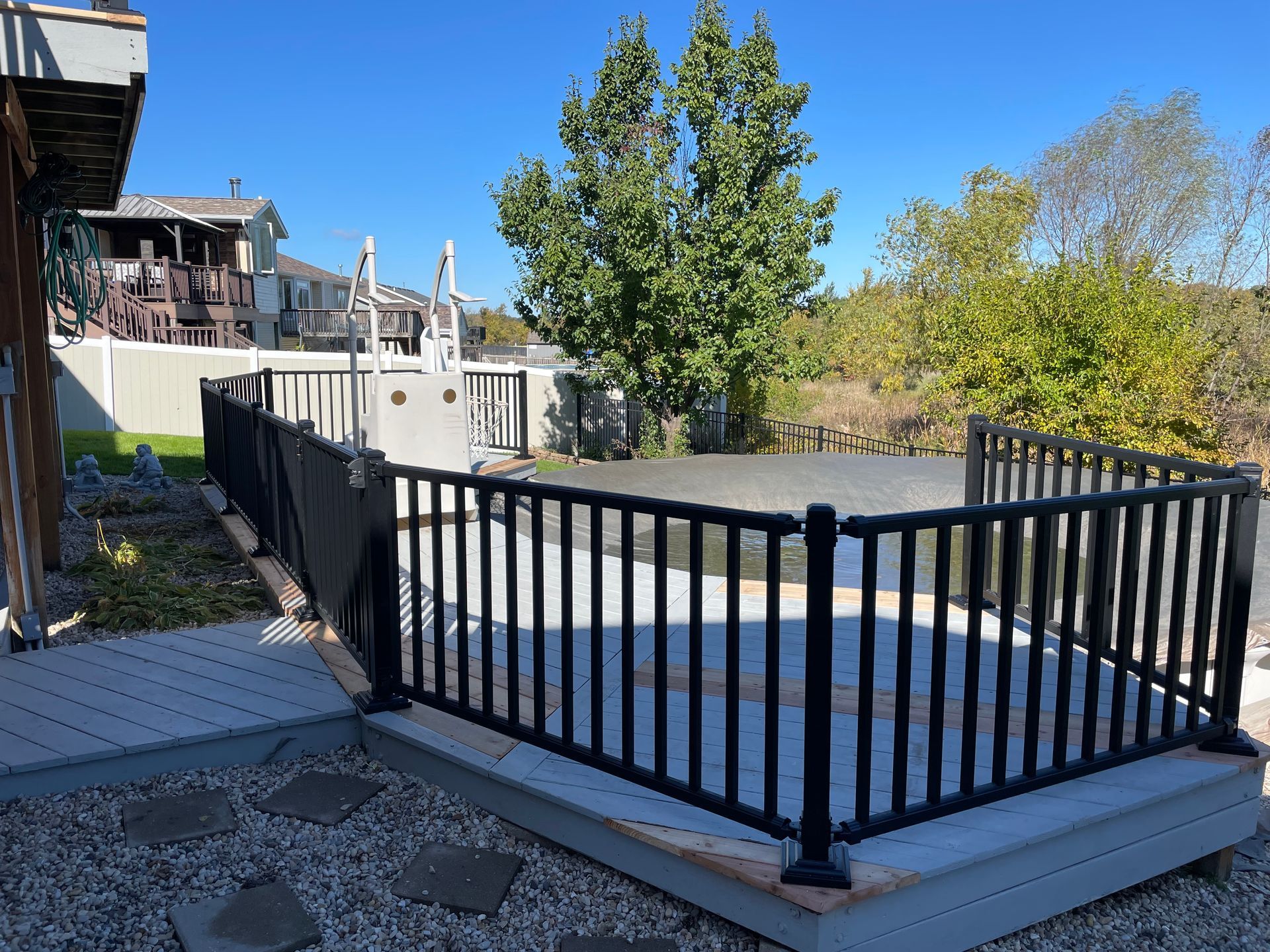 Black fenced deck area with surrounding landscaping and blue sky.