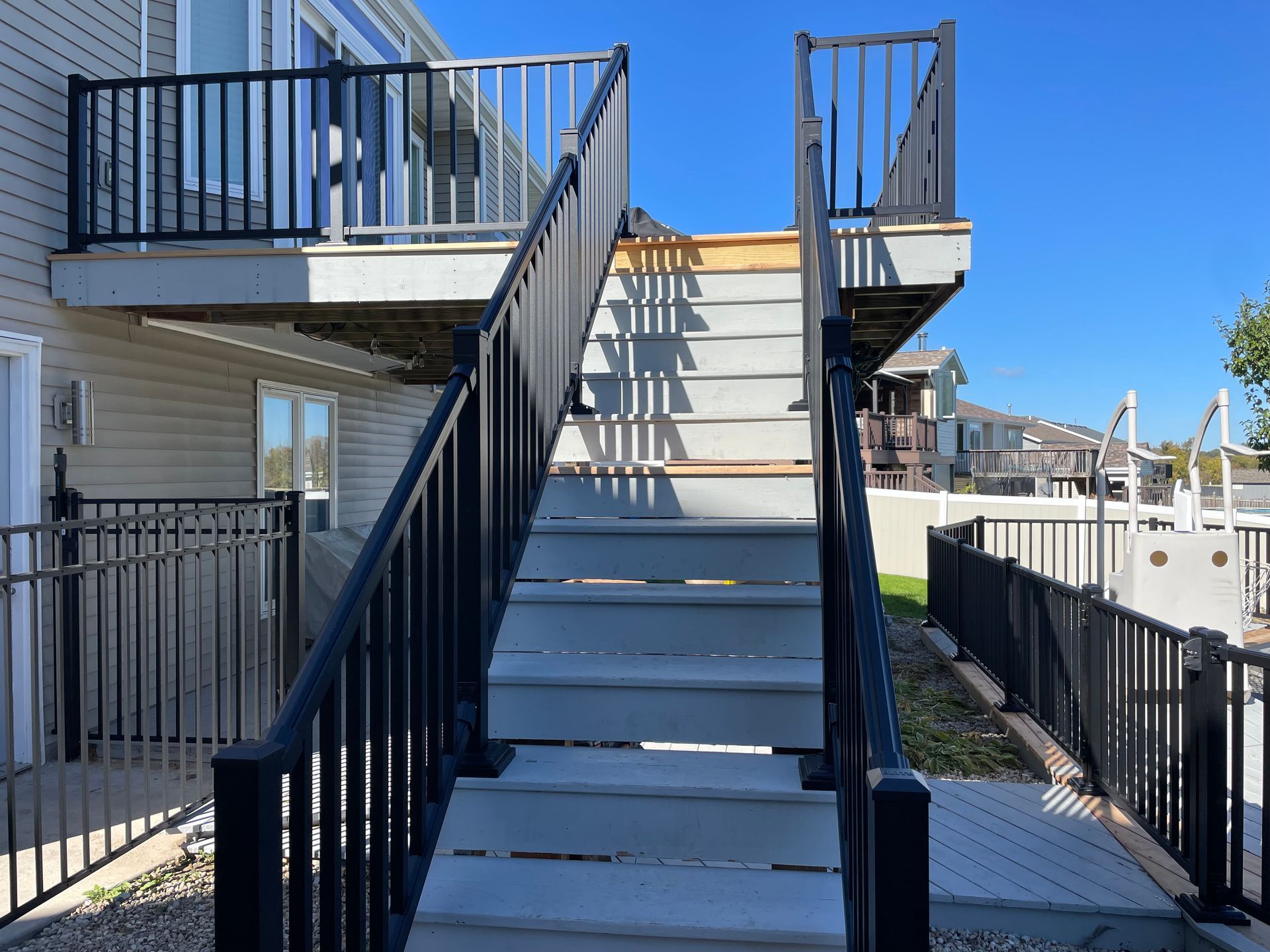 Outdoor staircase with black railings leading up to a deck. Gray steps against a clear sky.