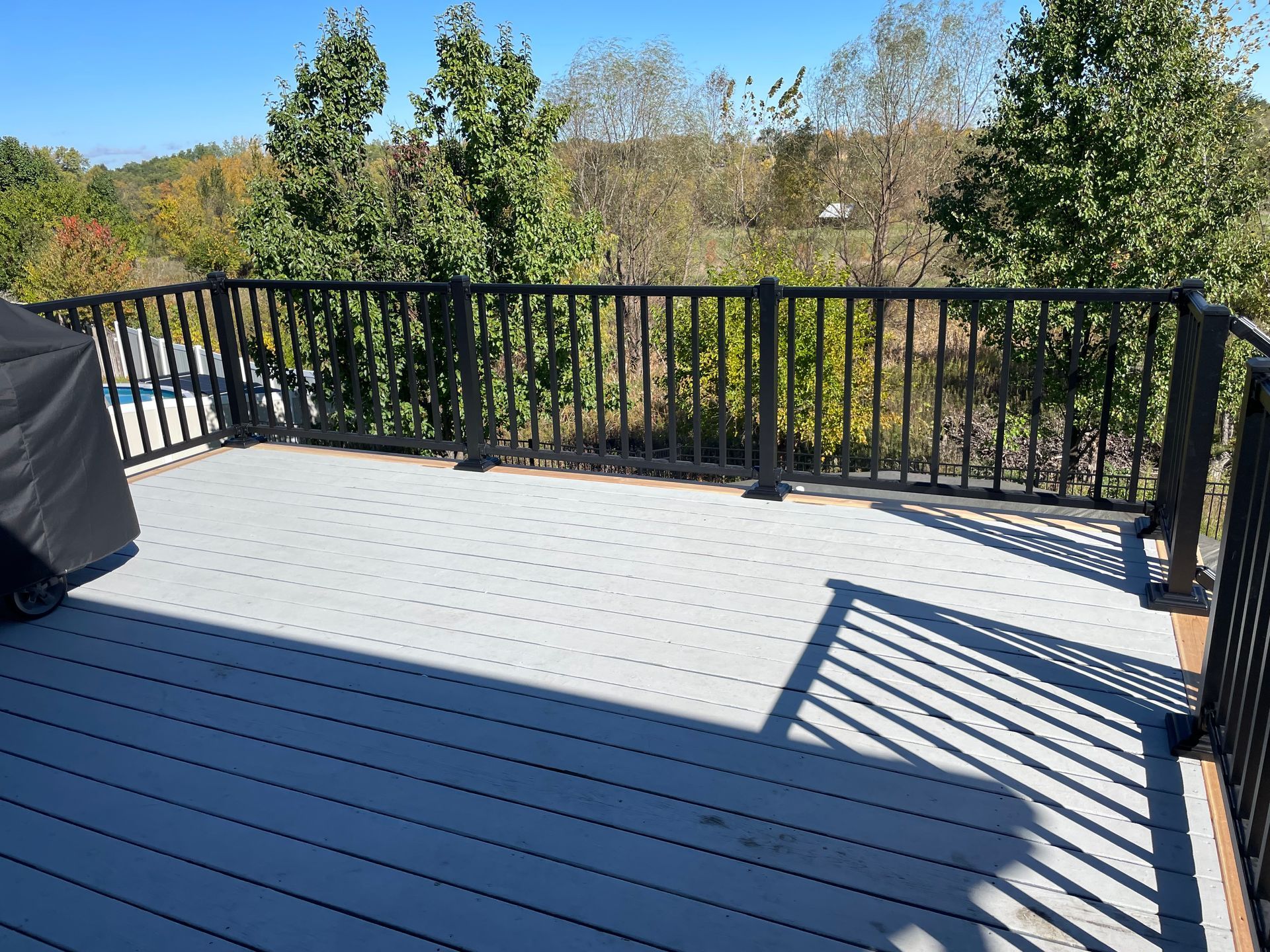 Gray composite deck with black railing overlooking trees.