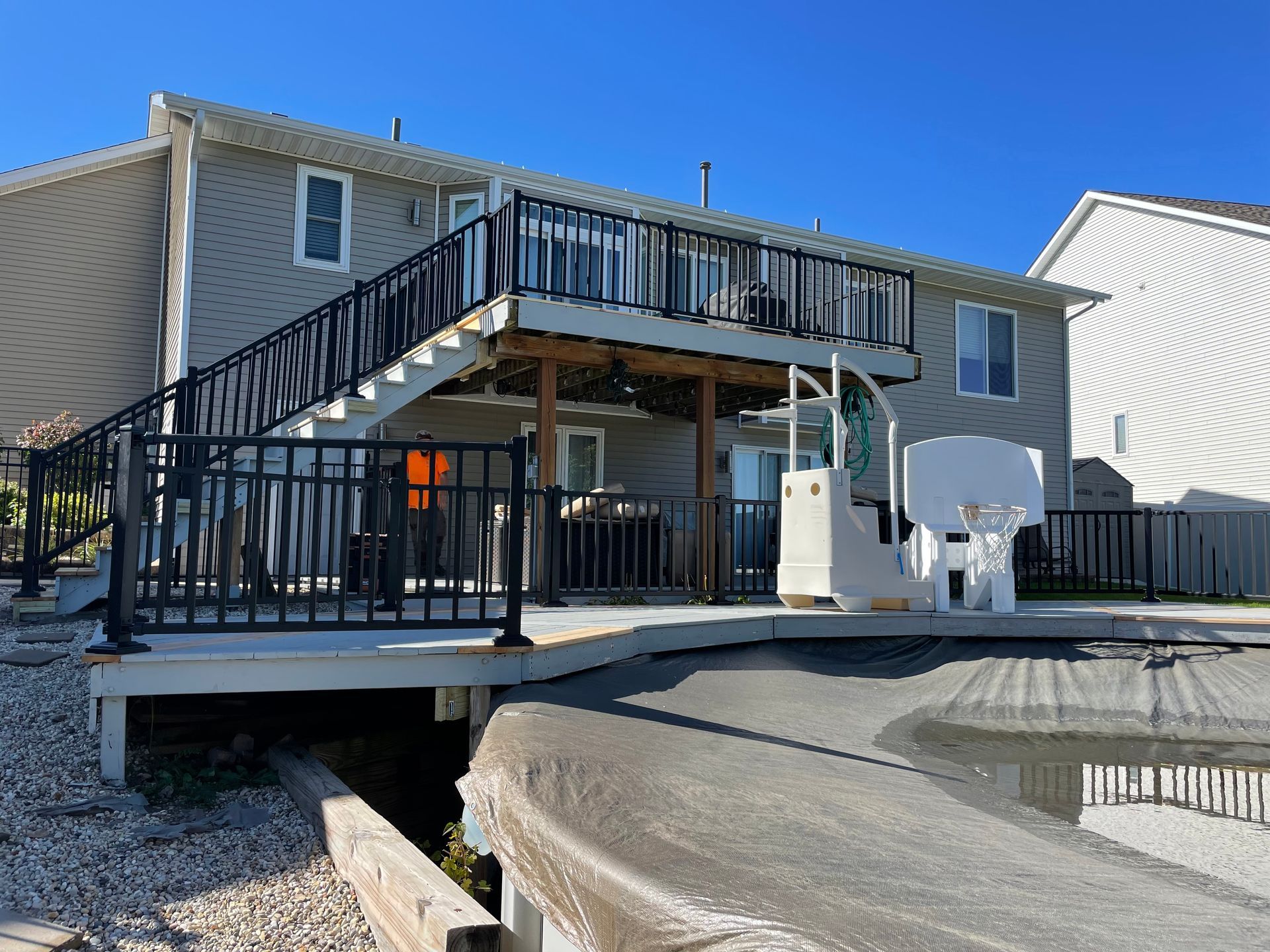 Back of a two-story house with a wooden deck, black railings, and a pool partially visible.