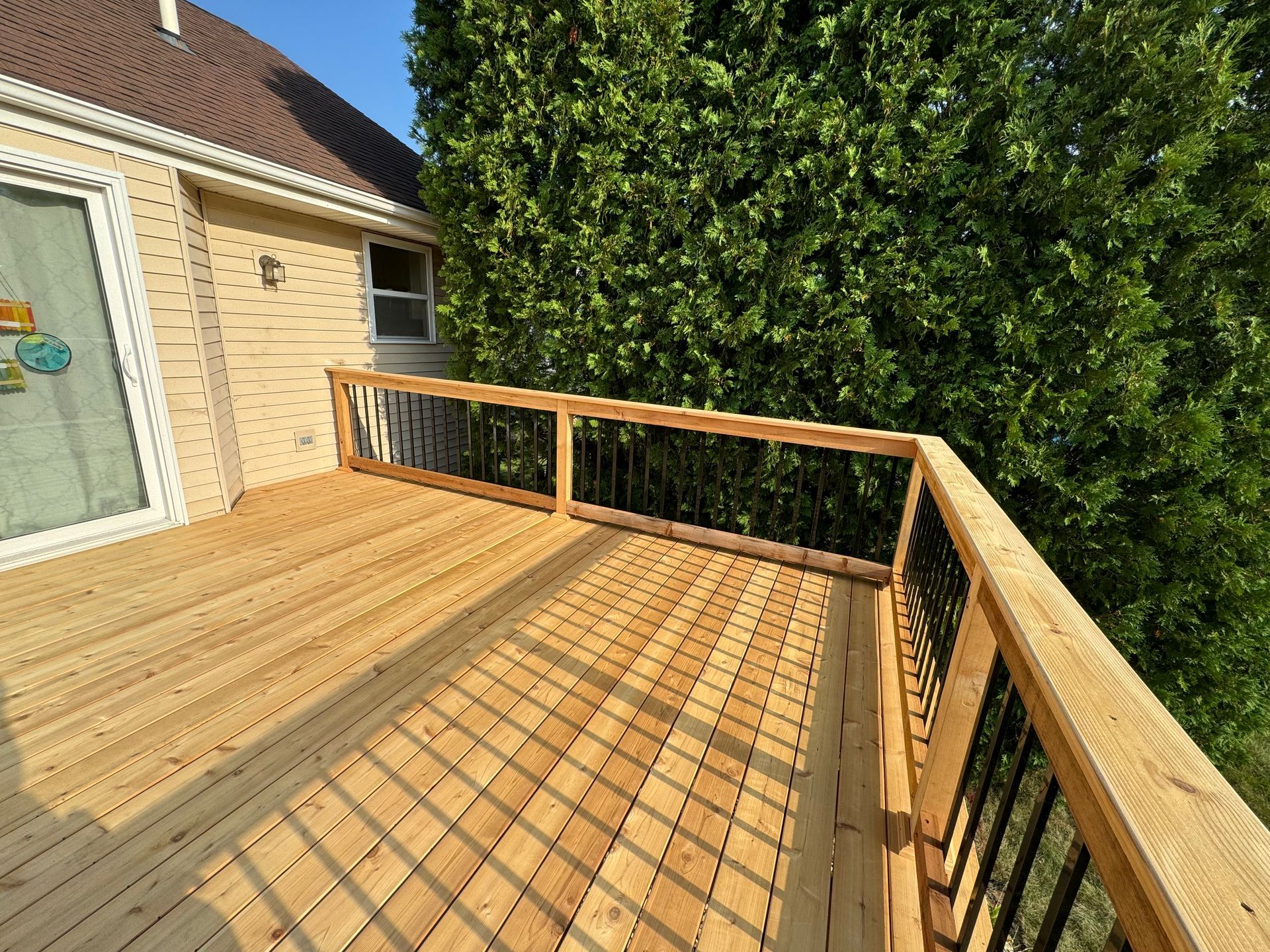 Wooden deck with black railings; side of a house with a window and a large green tree.