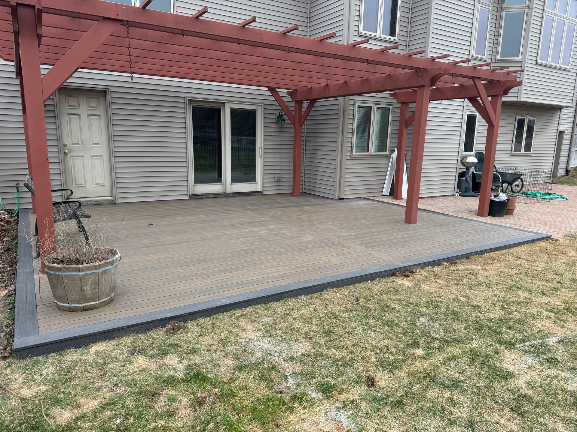 Backyard patio with red pergola, gray pavers, and a door, next to a grassy yard.