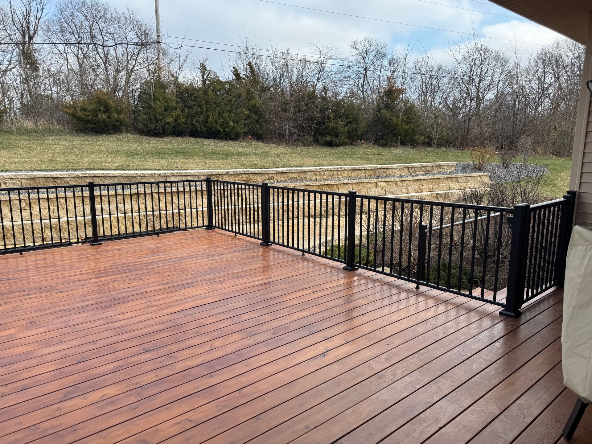 Wooden deck with black railing, overlooking a grassy yard and trees.
