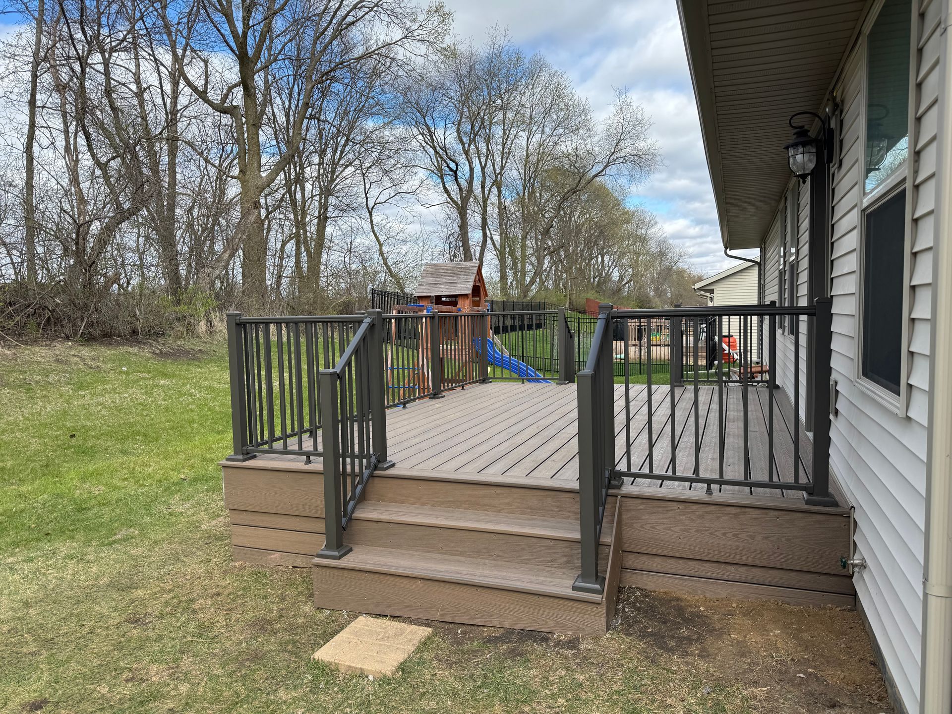 Deck with brown composite decking and dark metal railings. A play set is in the background.