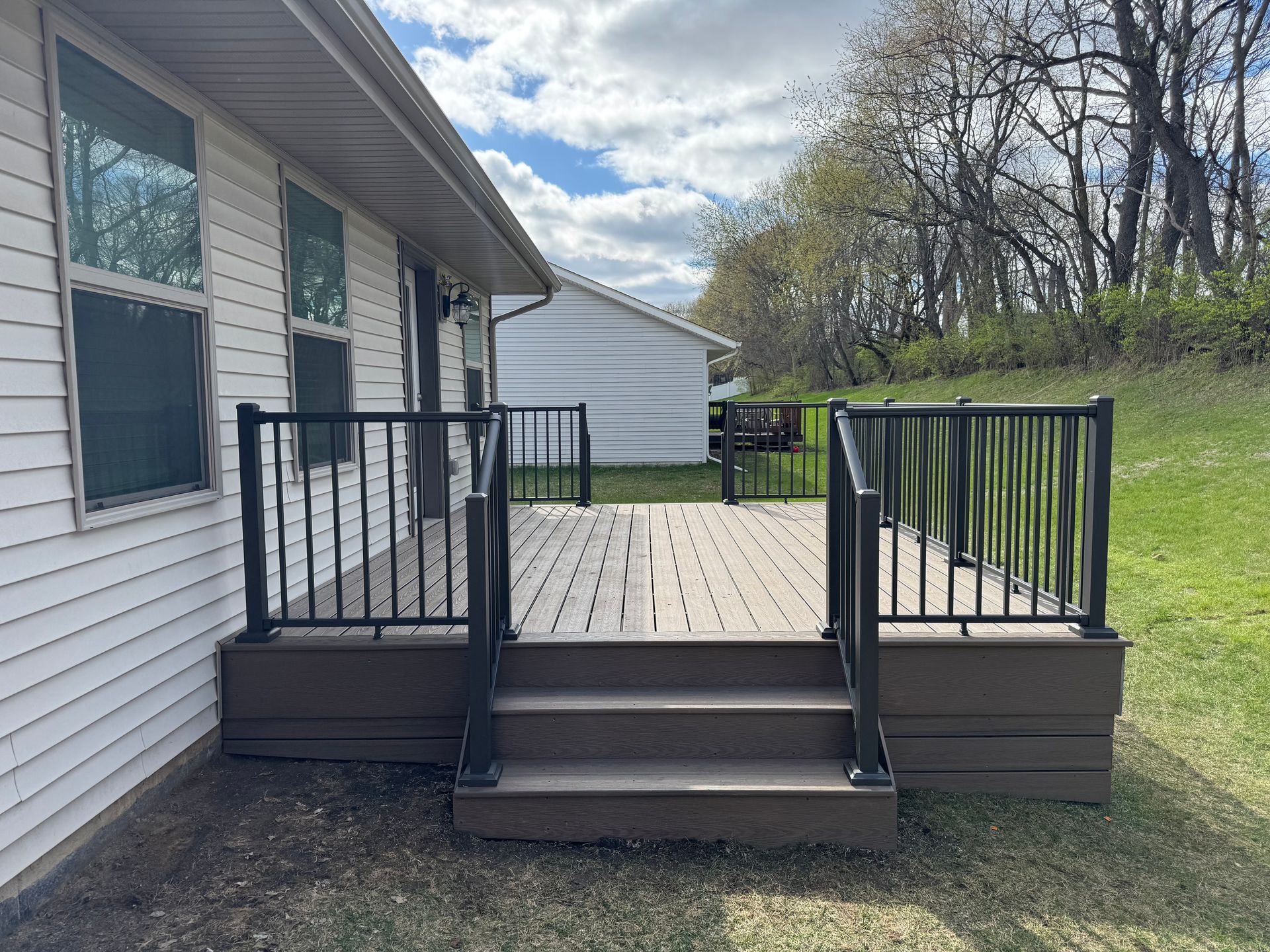 Brown deck with black railing and steps attached to a white house.