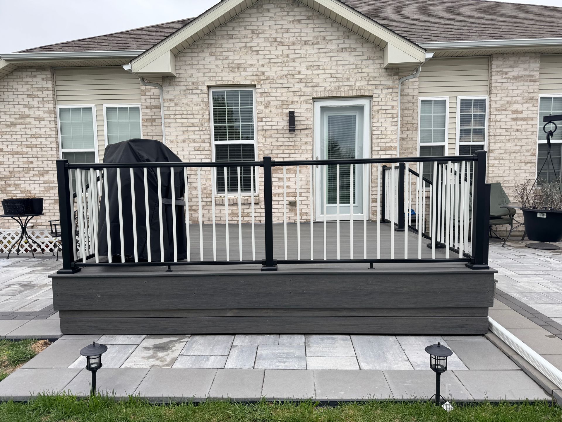 Backyard deck with dark gray composite, black railings, and white spindles. Brick house in the background.