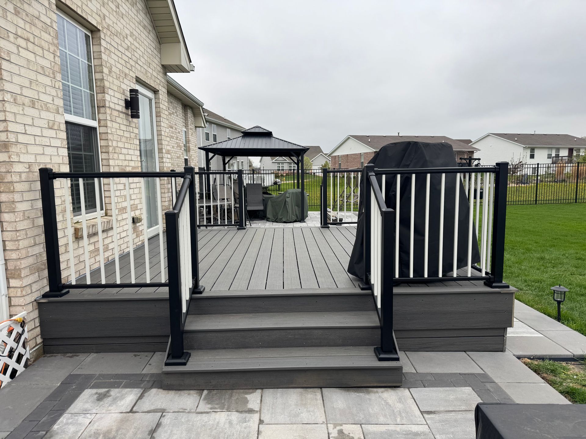 Deck with steps, composite decking, black and white railings, gazebo in backyard. Gray, cloudy sky.