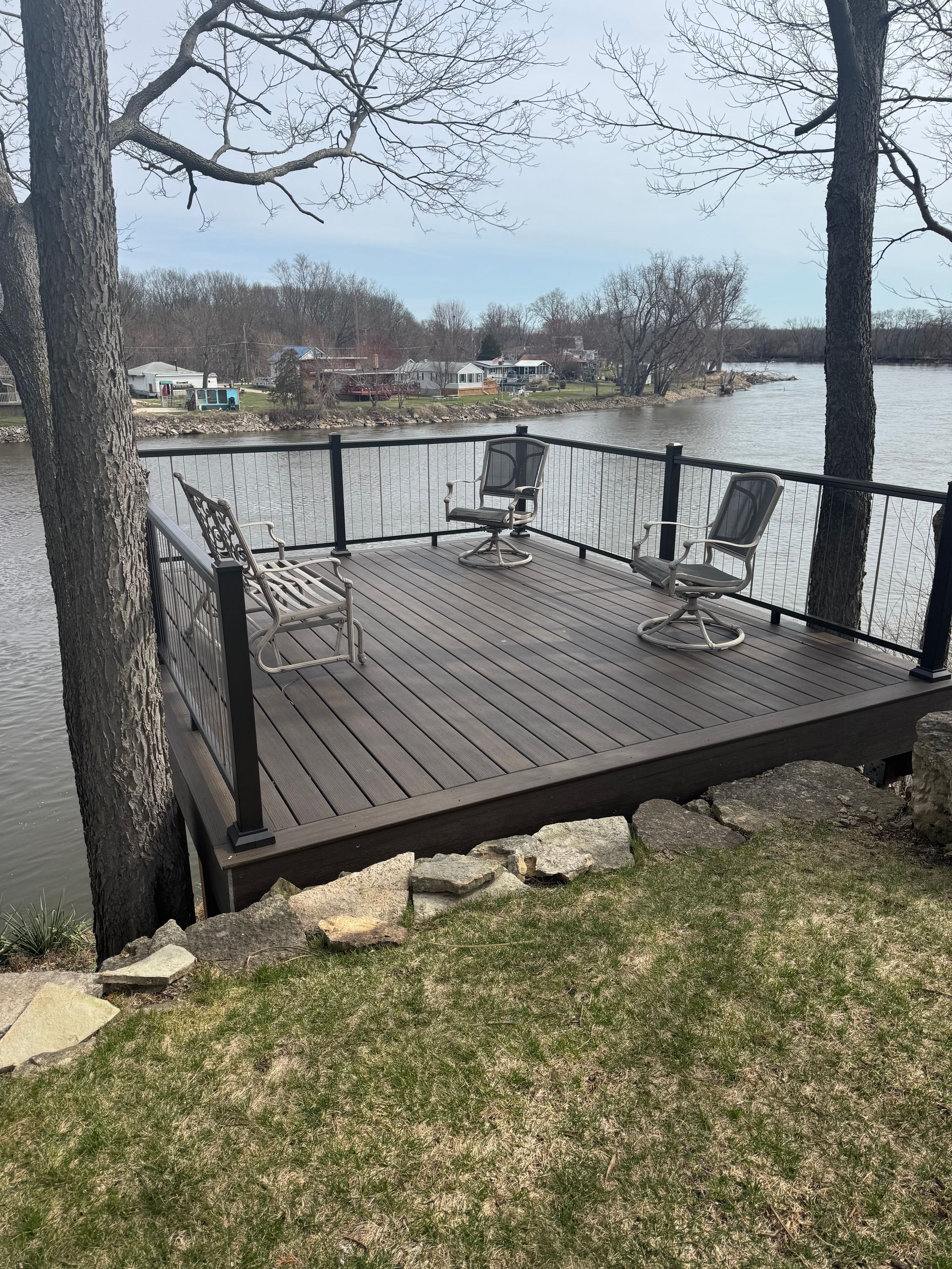 Wooden deck with chairs, black railing, and cable fencing overlooking water.