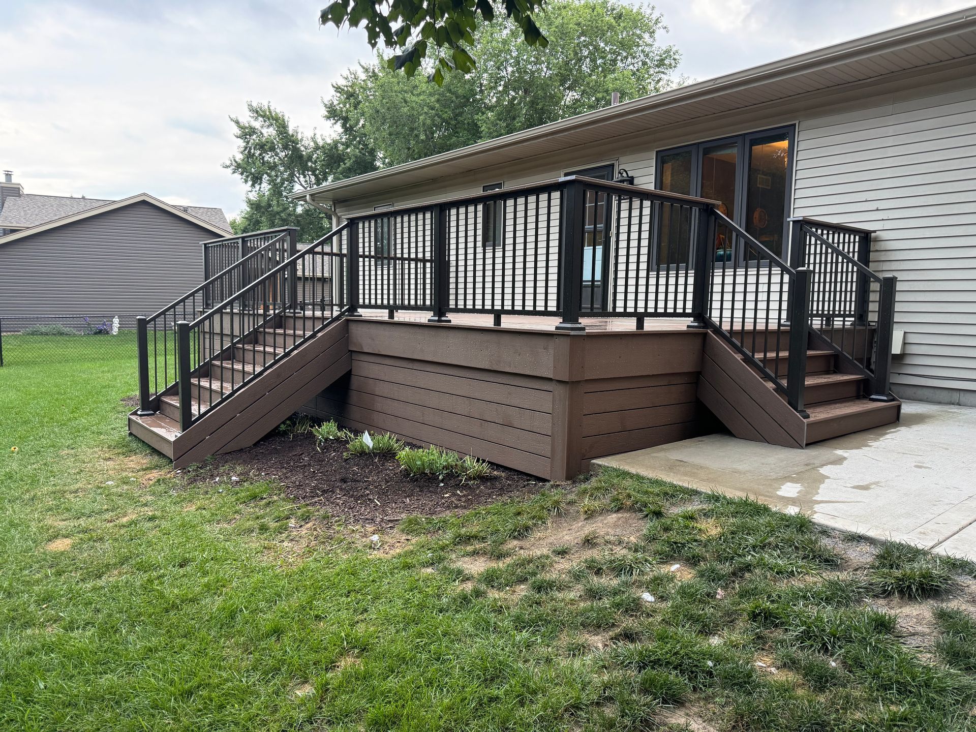 Brown composite deck with black railing and steps attached to a house with beige siding.
