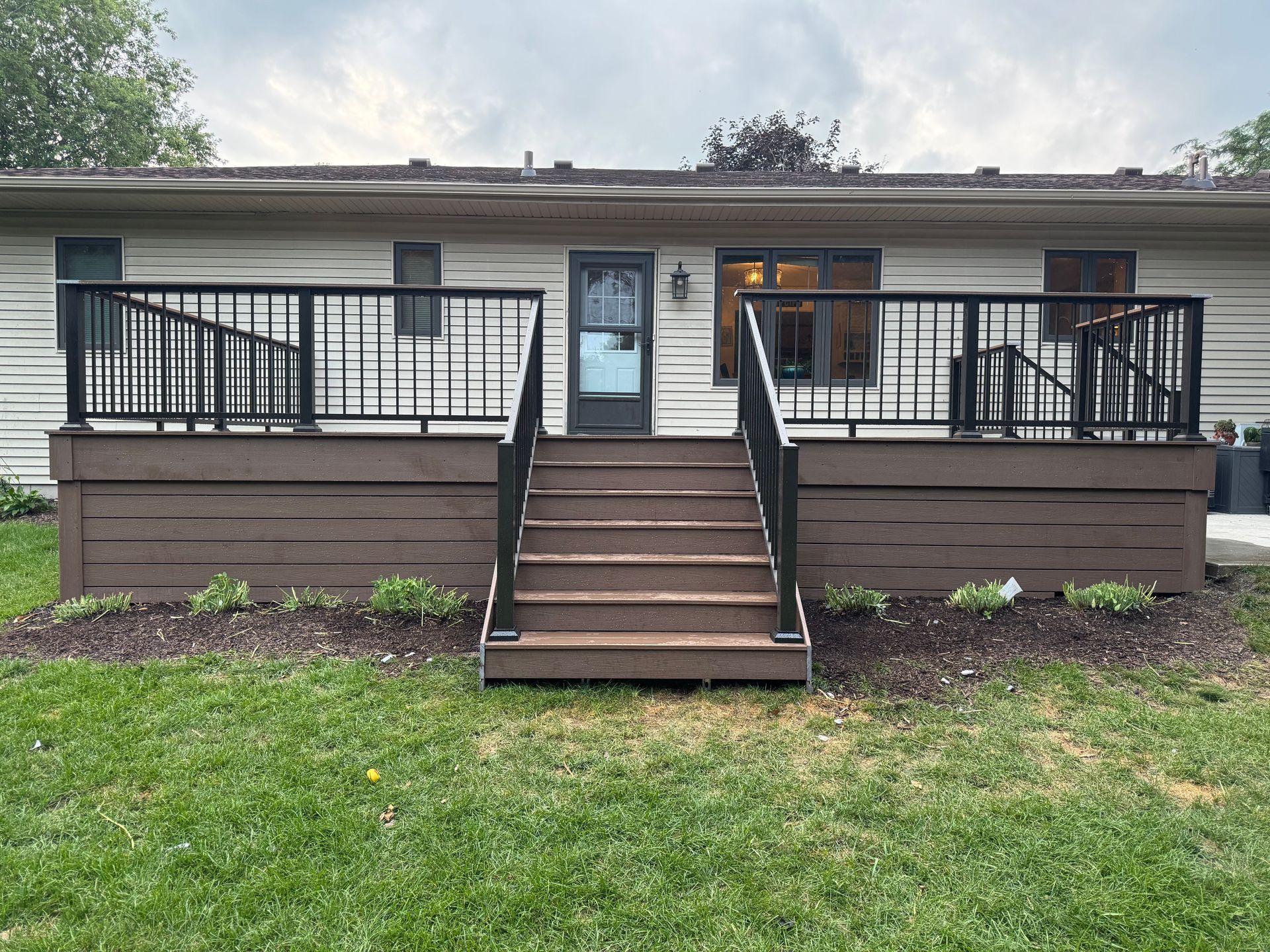 A brown wooden deck with black railings and steps leading to a back door.