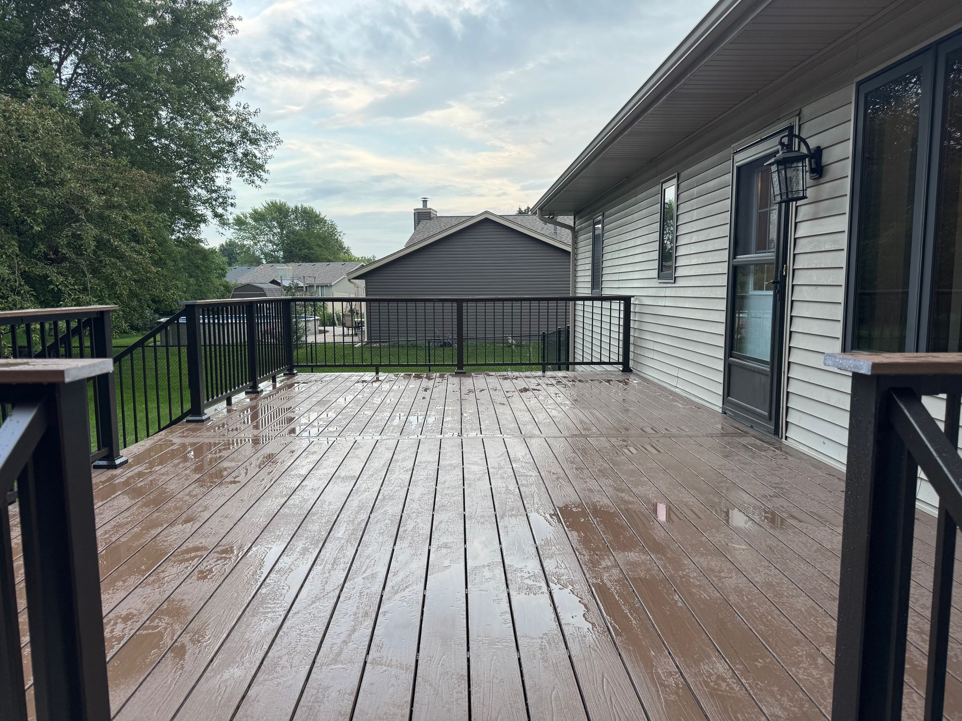 Wooden deck with black railings and house in the background. Overcast sky.