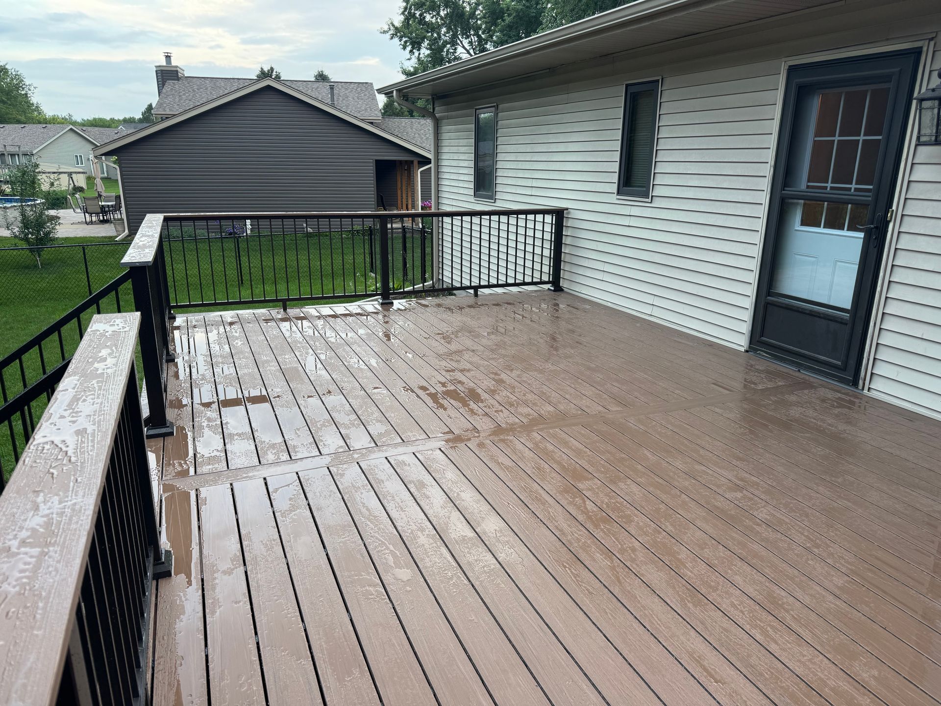 A wet, brown composite deck with black railings next to a house with white siding and a screened-in porch.