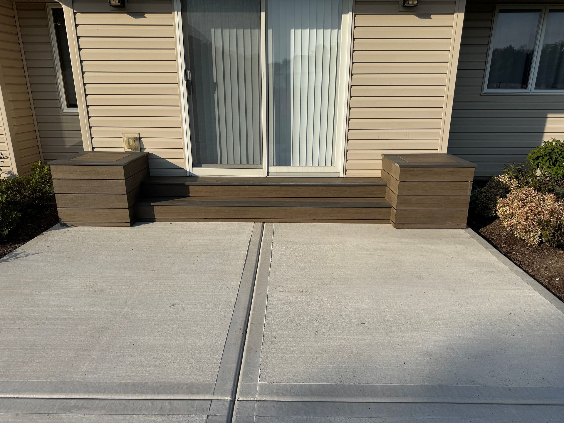 Concrete patio with steps leading to a sliding glass door; two rectangular planters flank the steps.