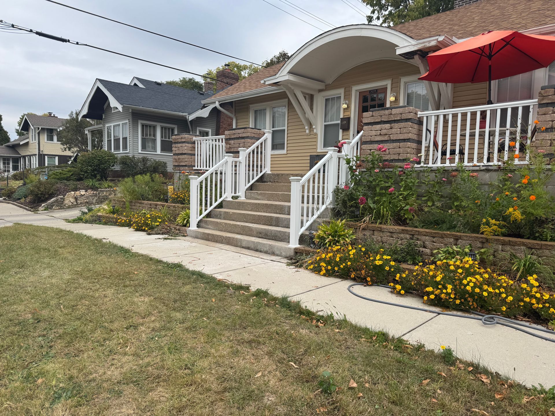 Row of houses with front steps, garden, and red umbrella on a porch. Sunny day.