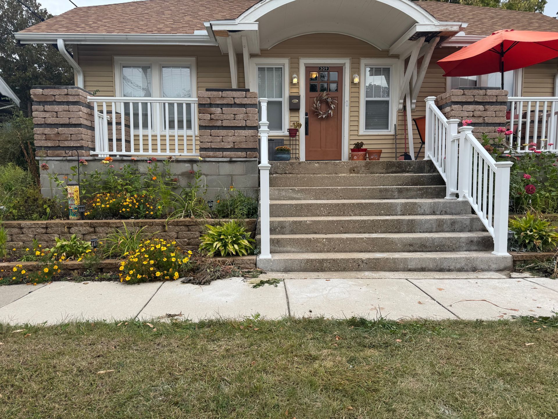 Tan house with stone and white trim, concrete steps, and a red umbrella.