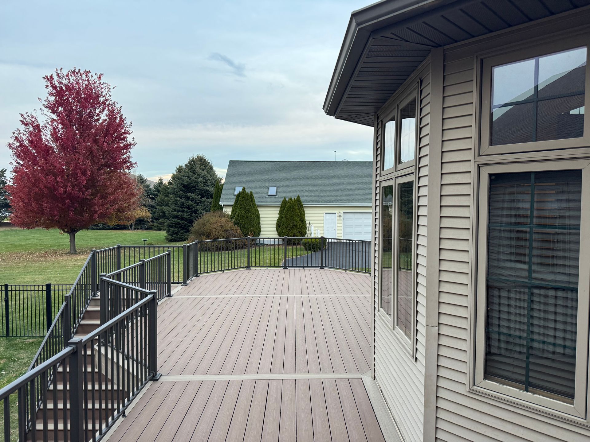Deck with composite boards, black railing, and red-leafed tree under an overcast sky.