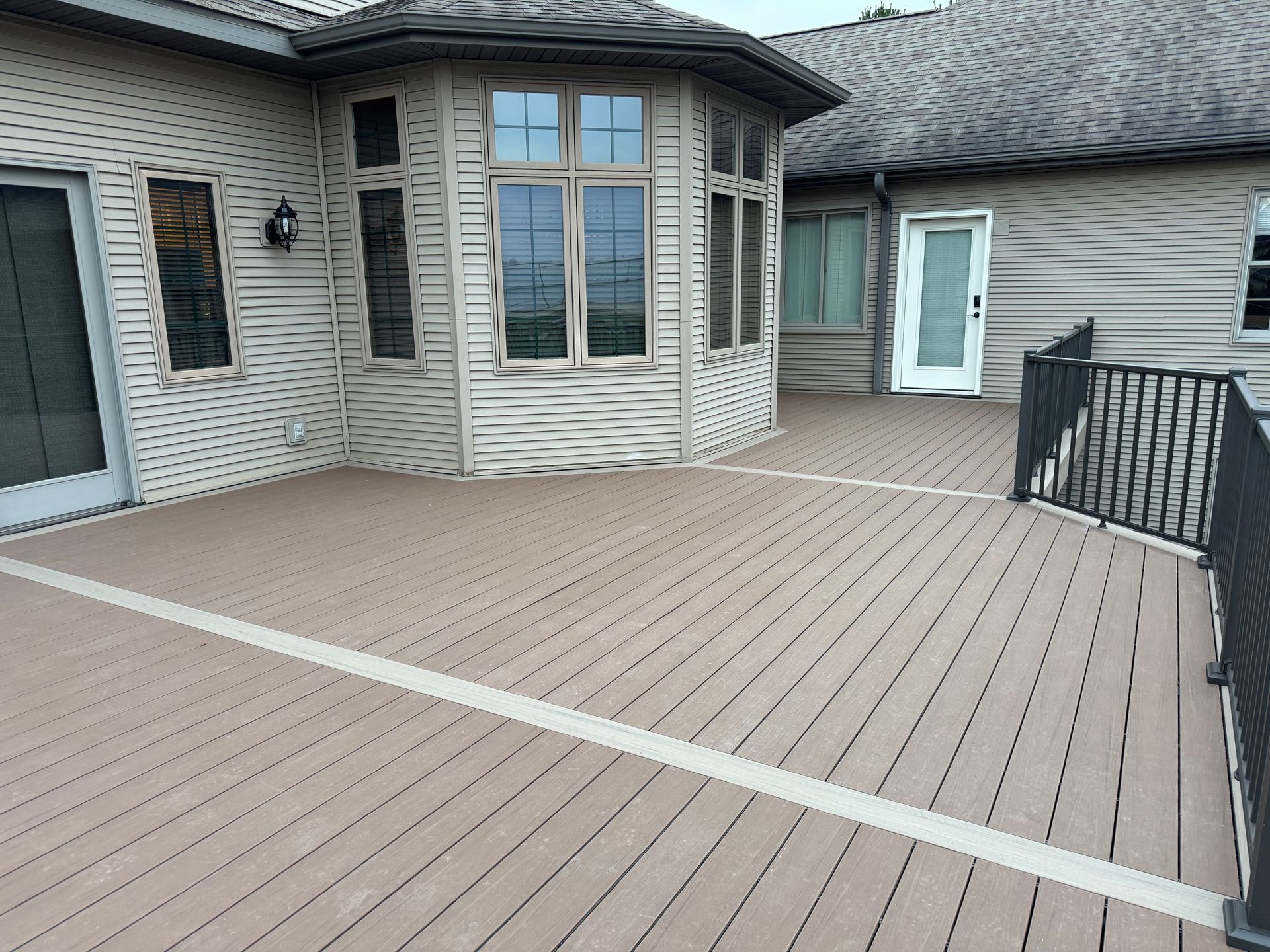 Composite deck with a house, windows, and black railing.