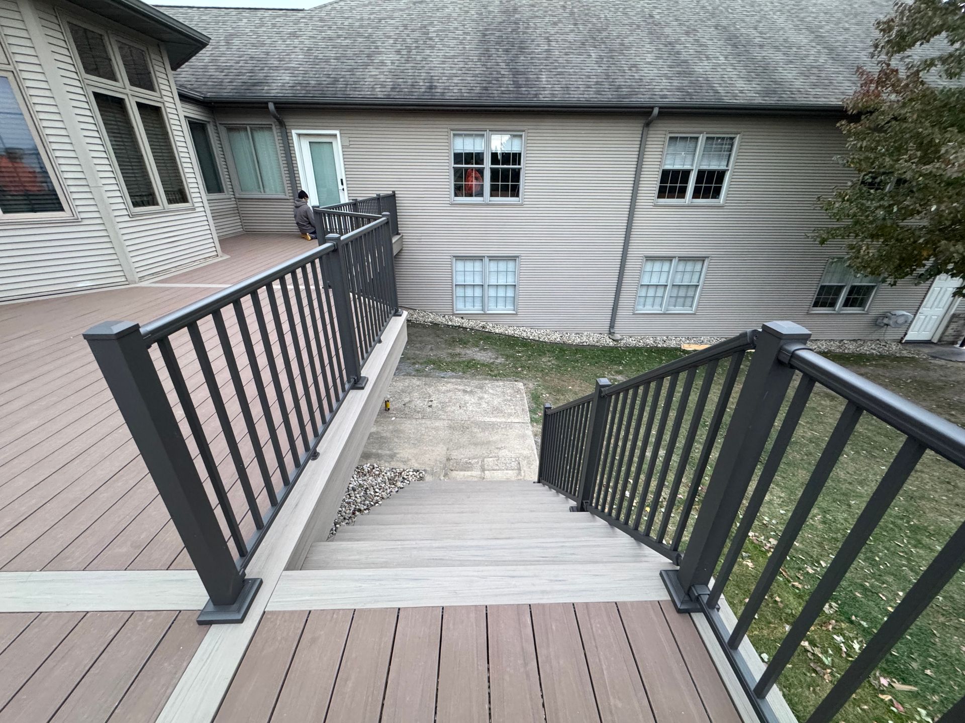 Deck with stairs leading down to a lower level, featuring dark railing and a house in the background.