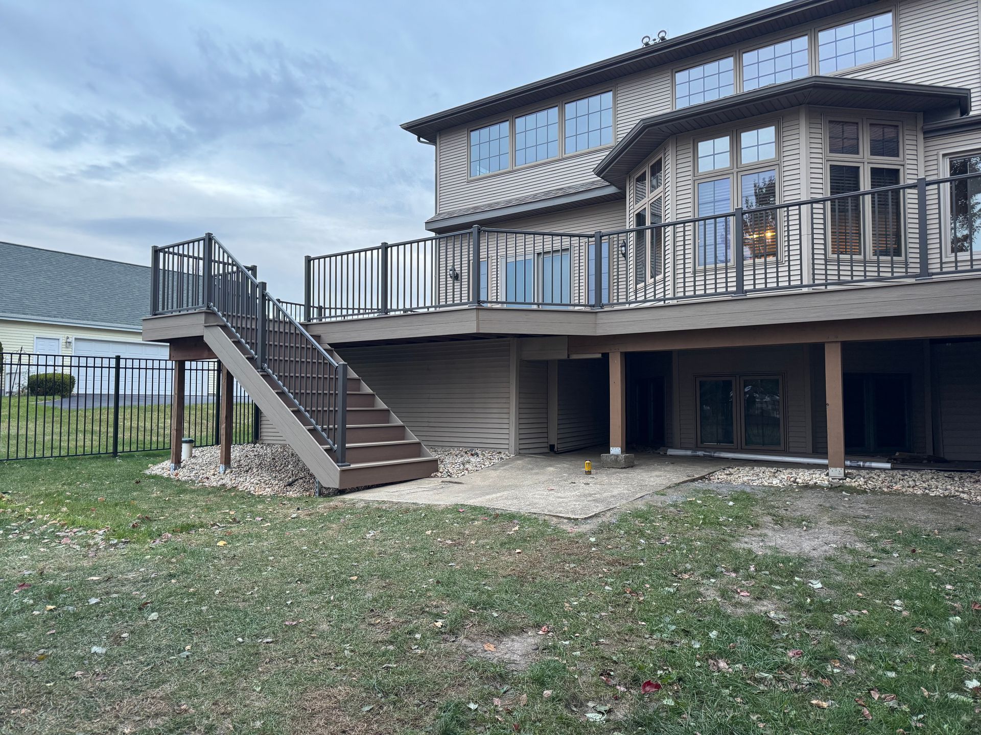 Exterior of a house with a multi-level deck, stairs, and a grassy yard under a cloudy sky.
