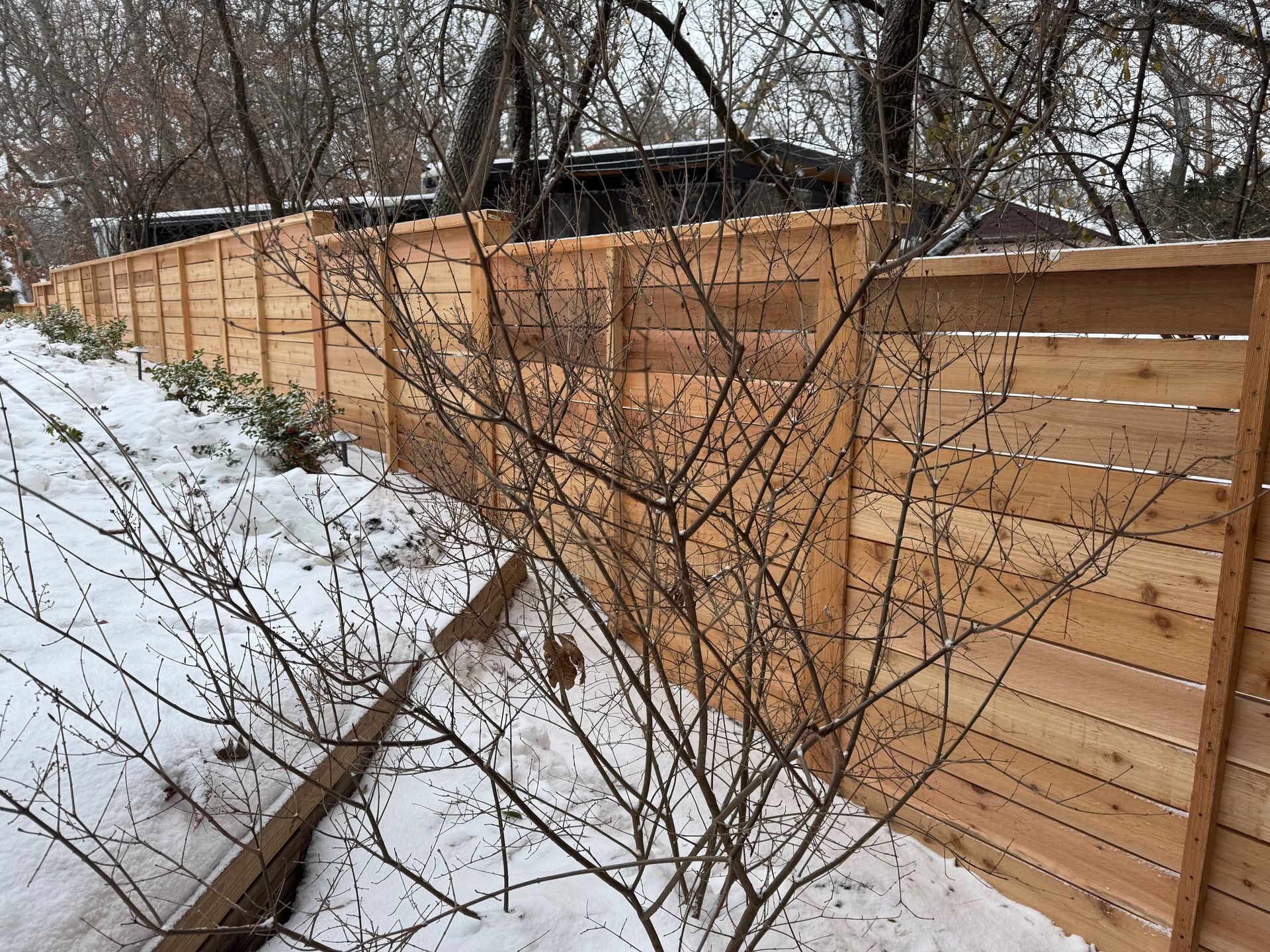 Wooden fence with a snow-covered yard and bare trees.