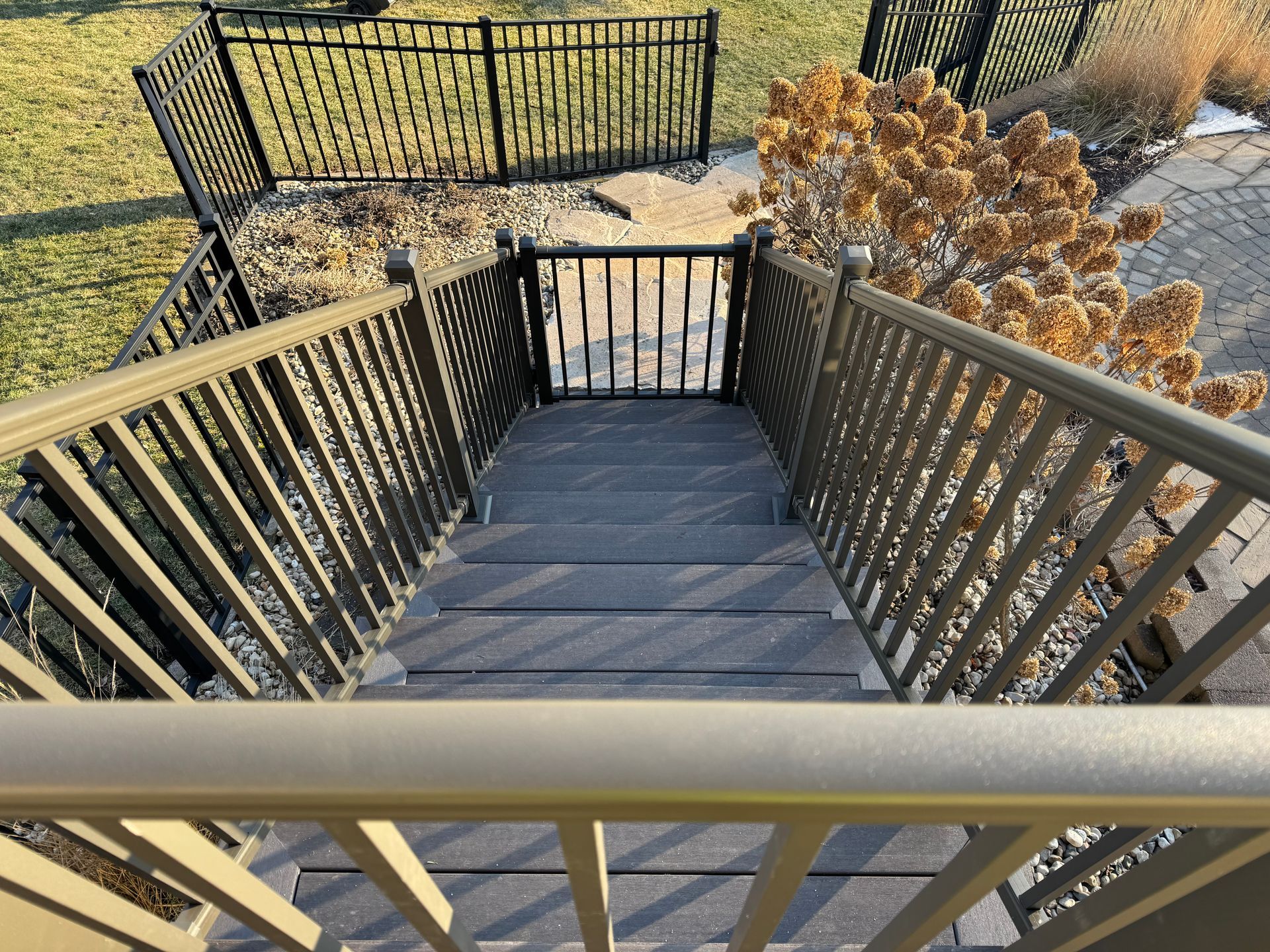 Staircase with tan railings and gray steps, leading down to a gate and black fence in a yard.