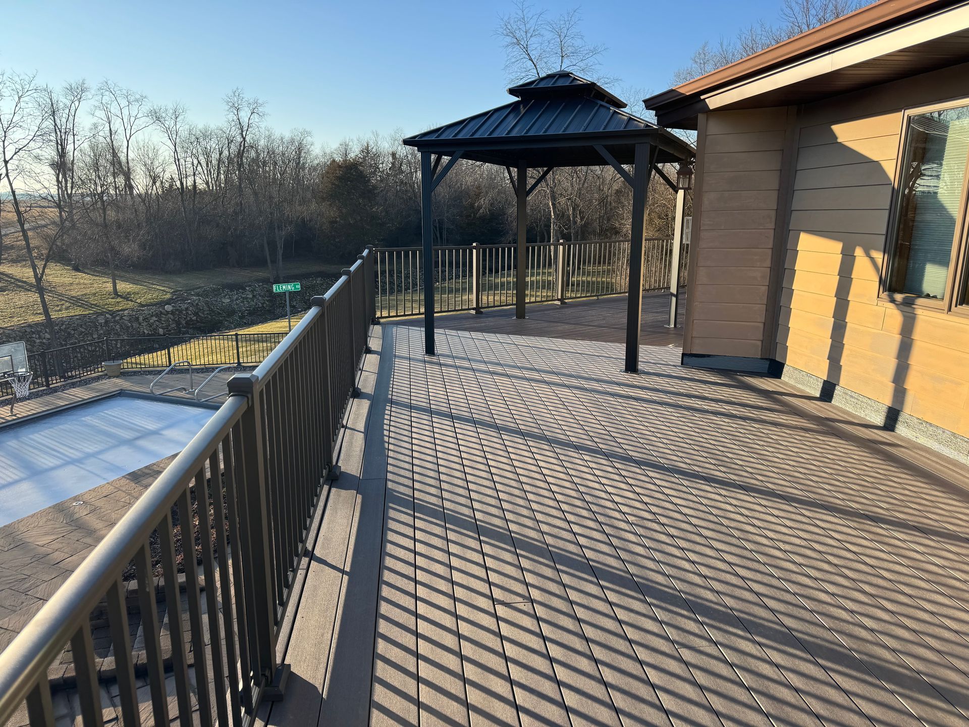 Wooden deck with gazebo, railing, and building; sunny outdoor setting.