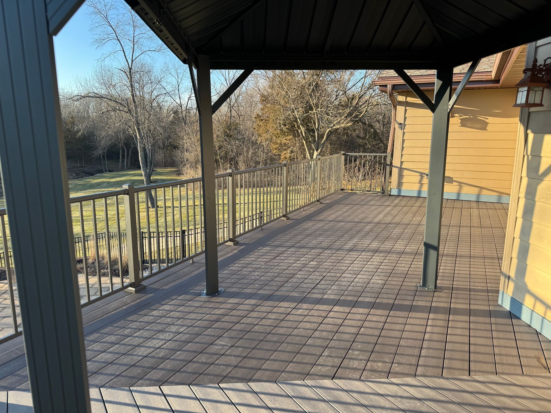 Gazebo covered deck with metal railing overlooking a yard with trees under a blue sky.