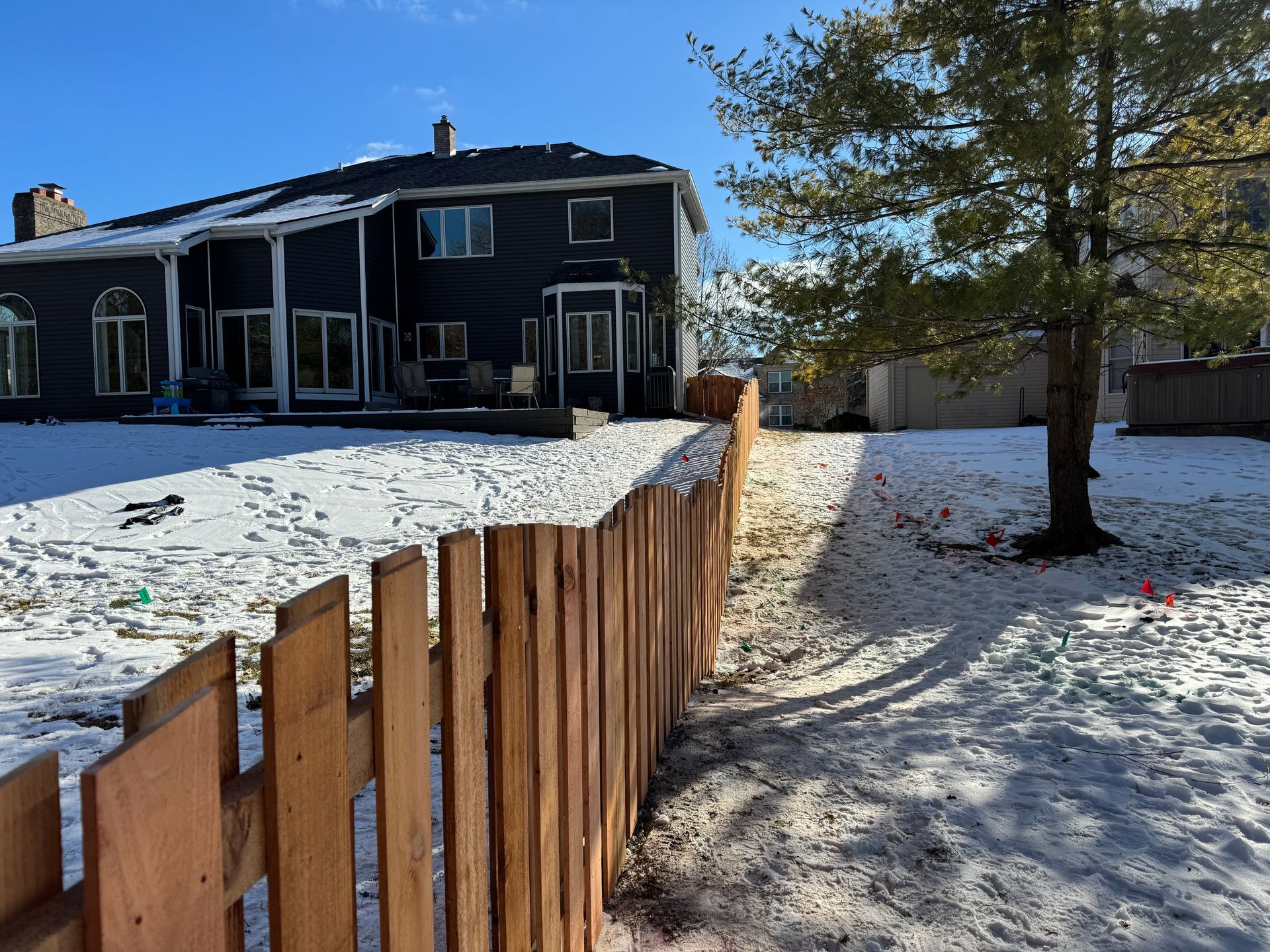Snowy backyard with wooden fence and dark house.