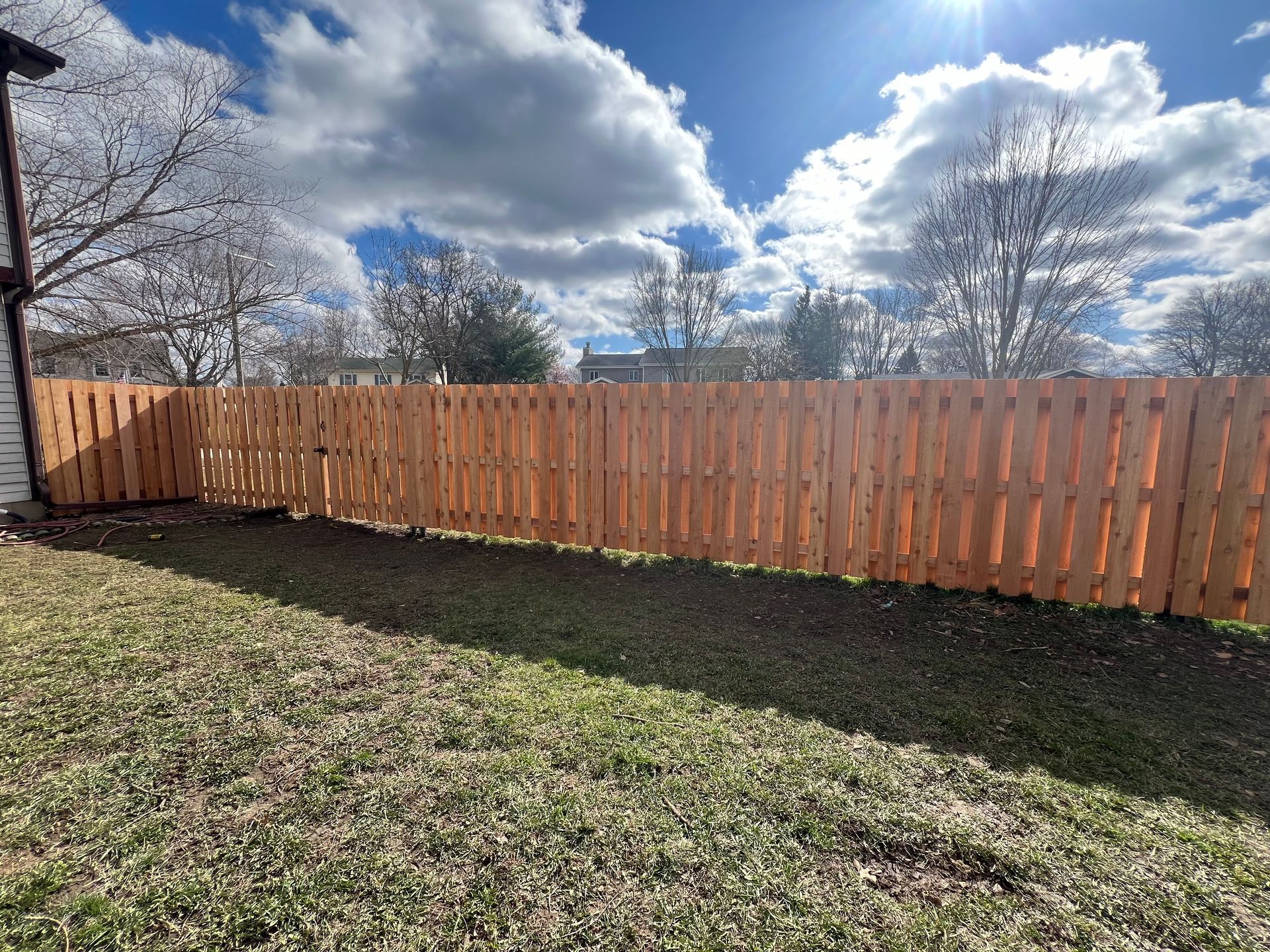 Wooden fence in a backyard under a partly cloudy, sunny sky.