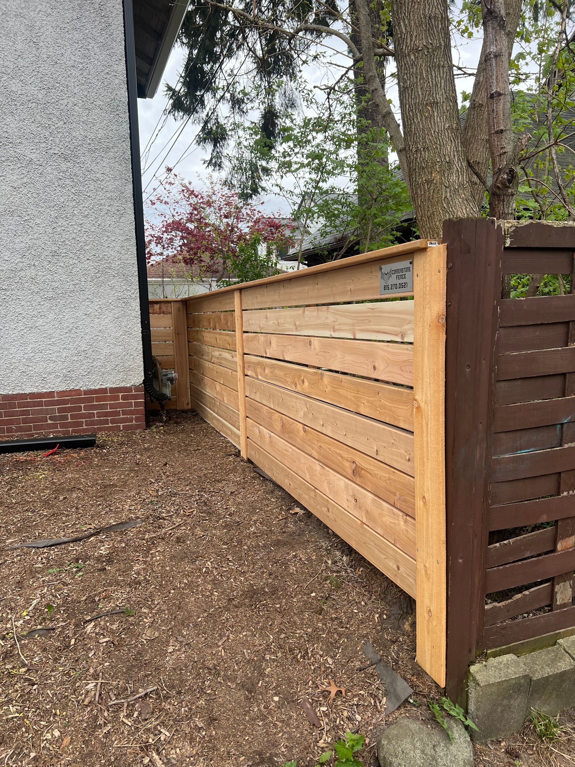 A wooden fence with horizontal planks next to a building and a tree.