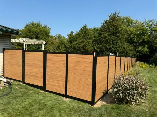 Brown privacy fence with black framing in a grassy backyard.