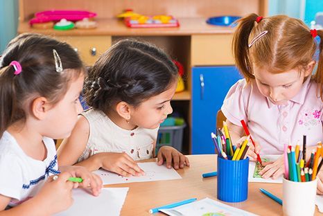 A group of young girls are sitting at a table drawing with pencils