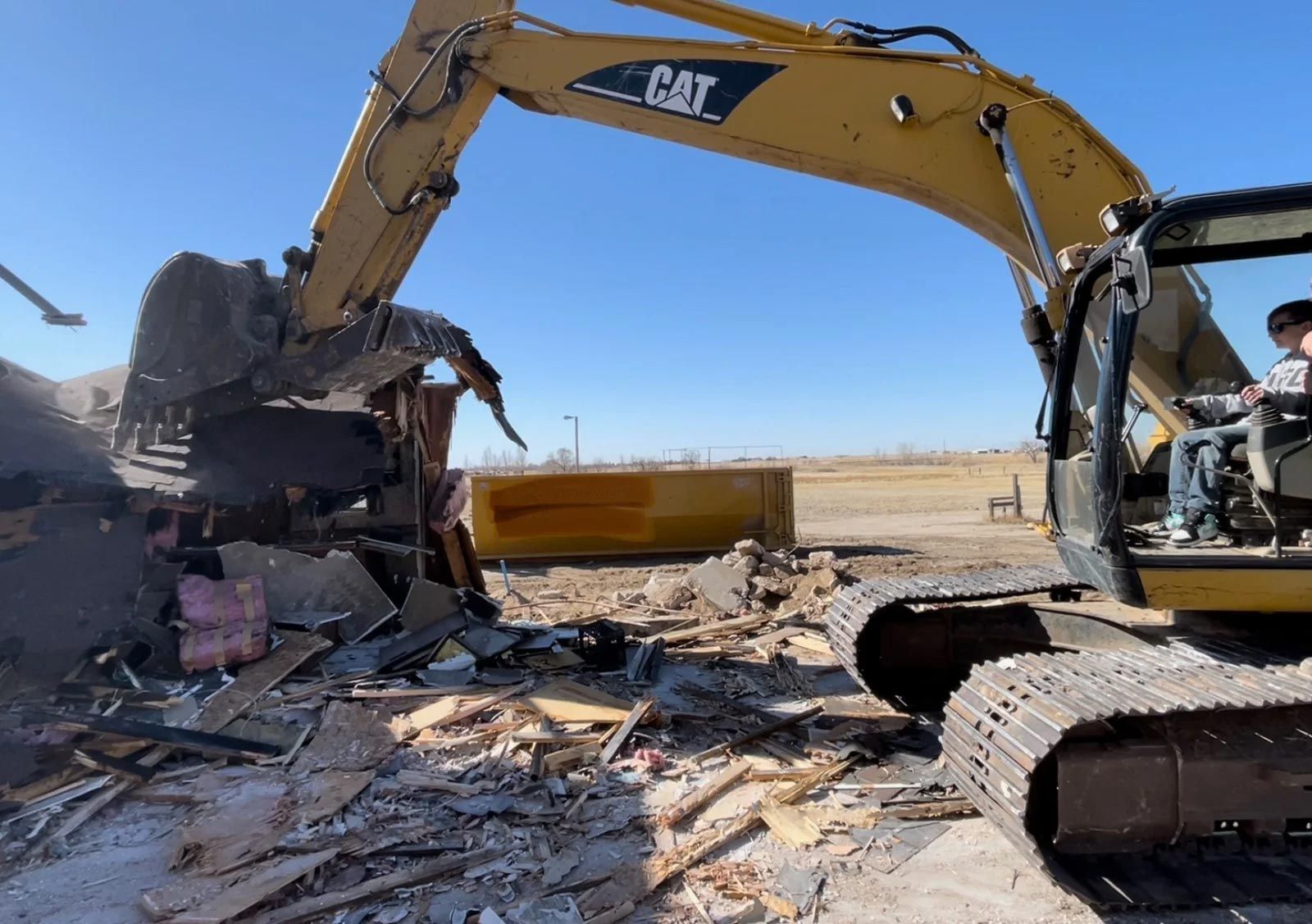 A cat excavator is demolishing a building in a field.