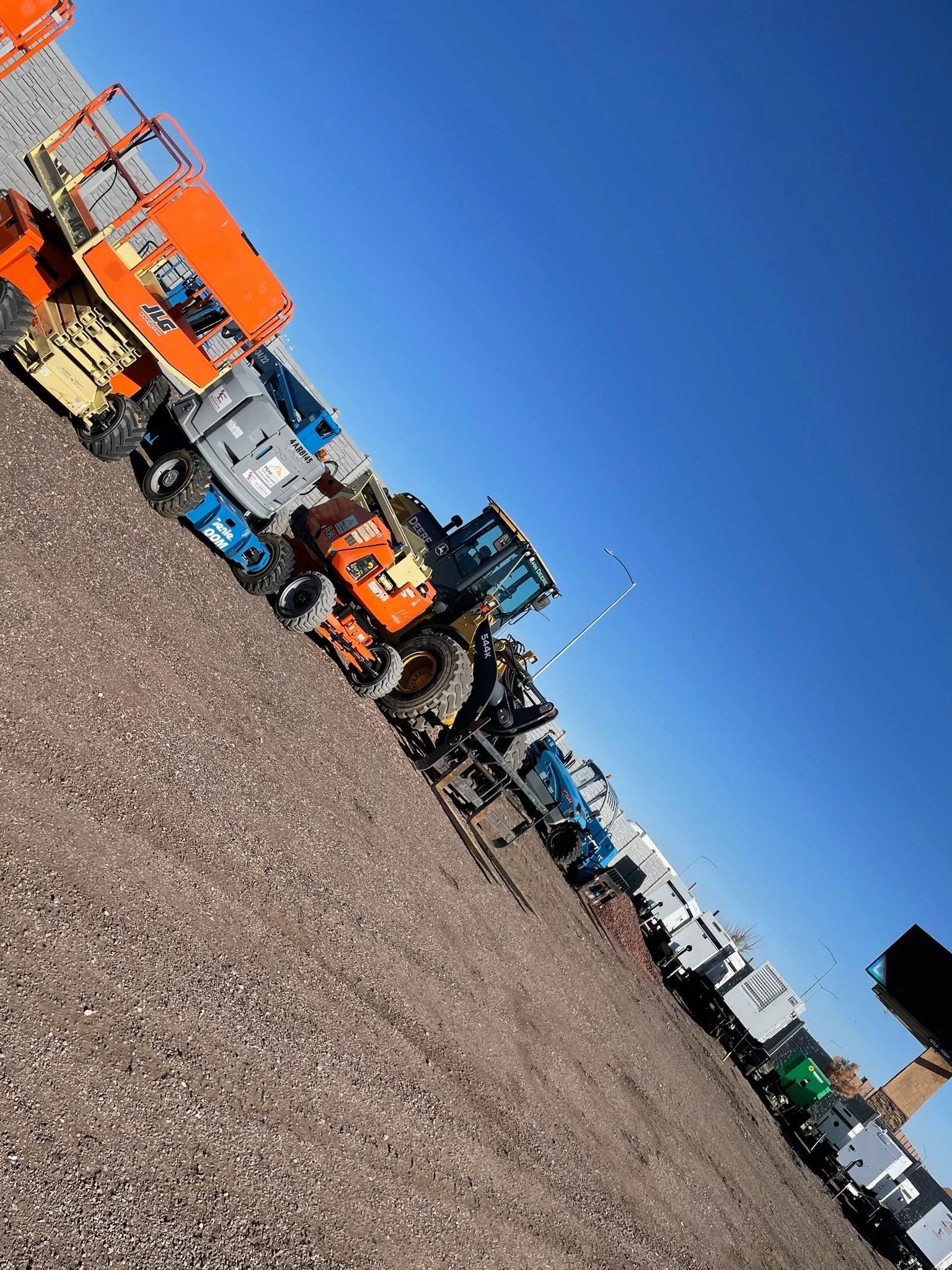A row of construction vehicles are parked in a gravel lot.