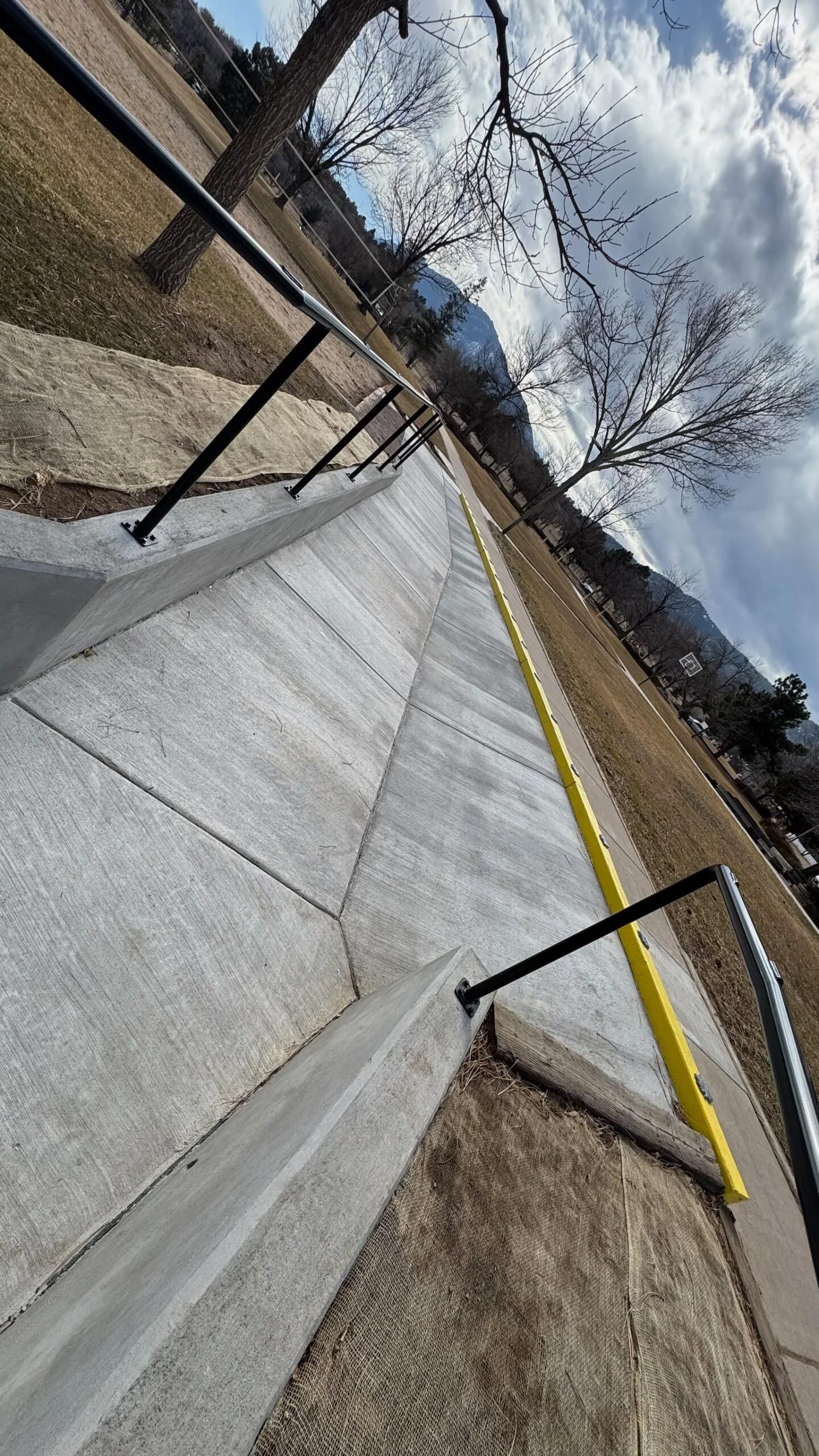 A concrete sidewalk with a yellow line on it and a railing.
