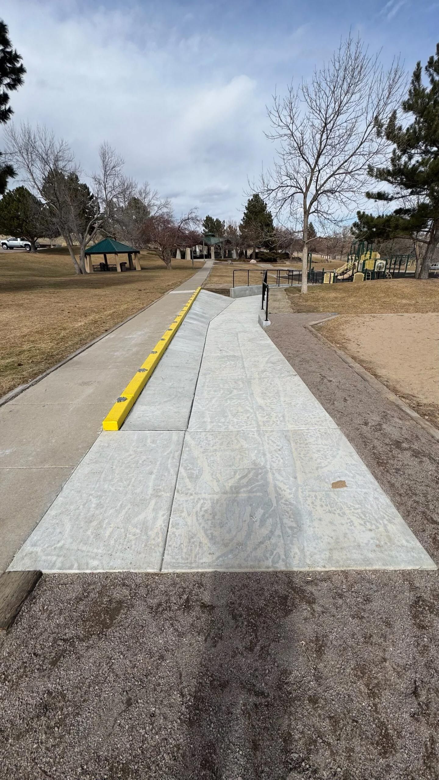 A concrete walkway with a yellow curb in a park.