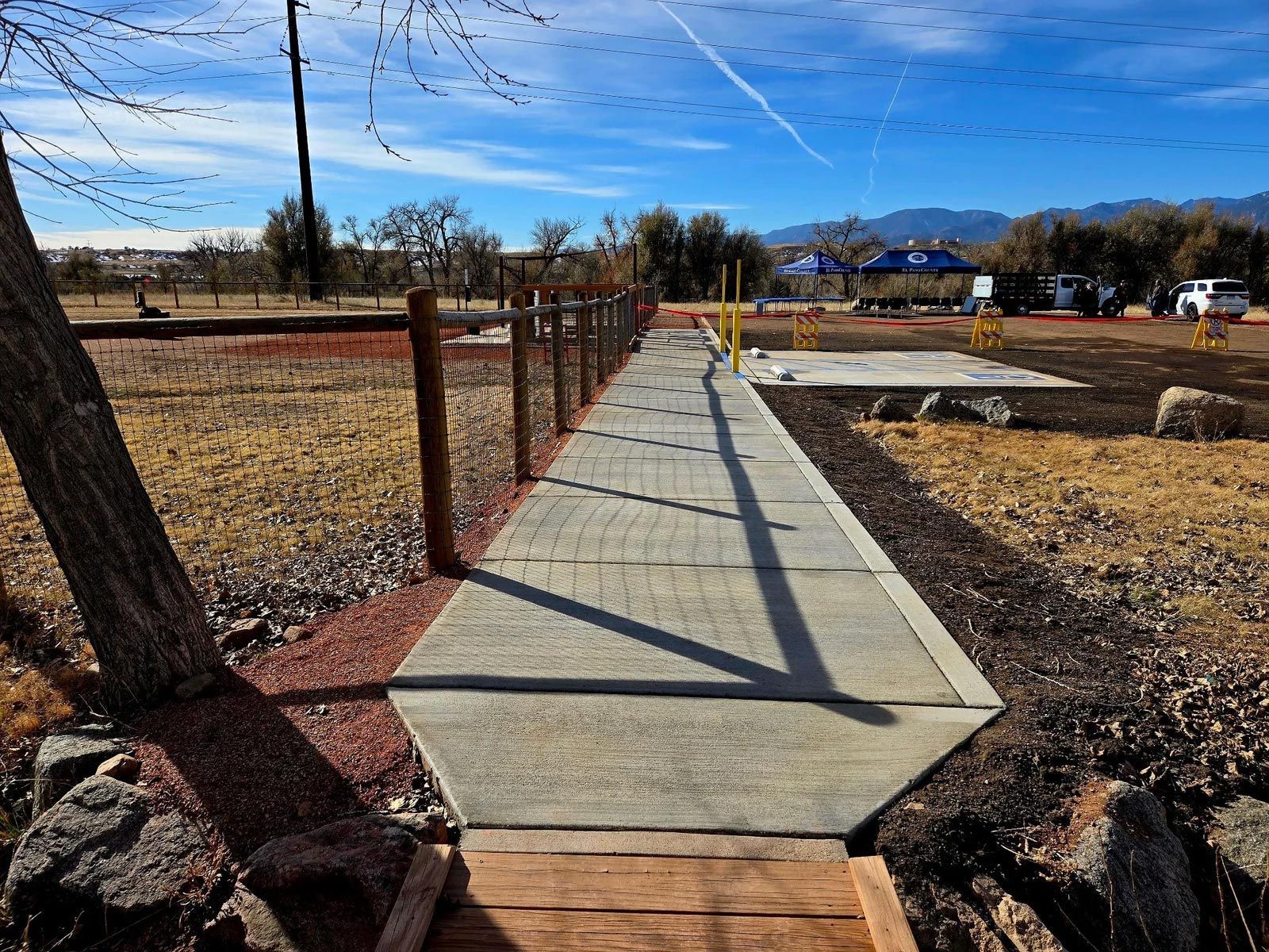 A concrete walkway leading to a wooden bridge in a field.
