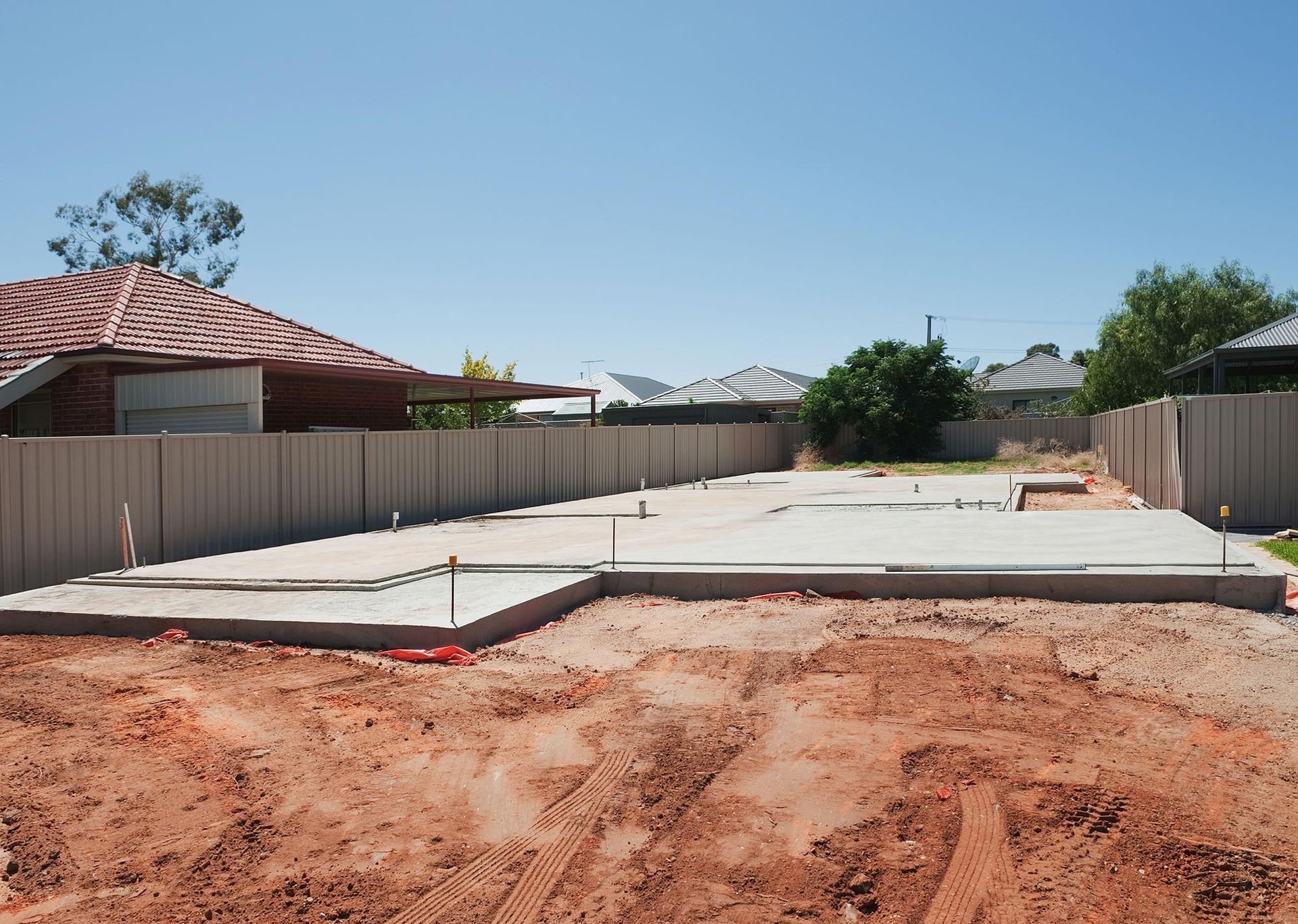 A concrete foundation is being built on a dirt field in front of a house.
