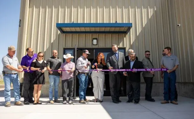 A group of people are cutting a purple ribbon in front of a building.