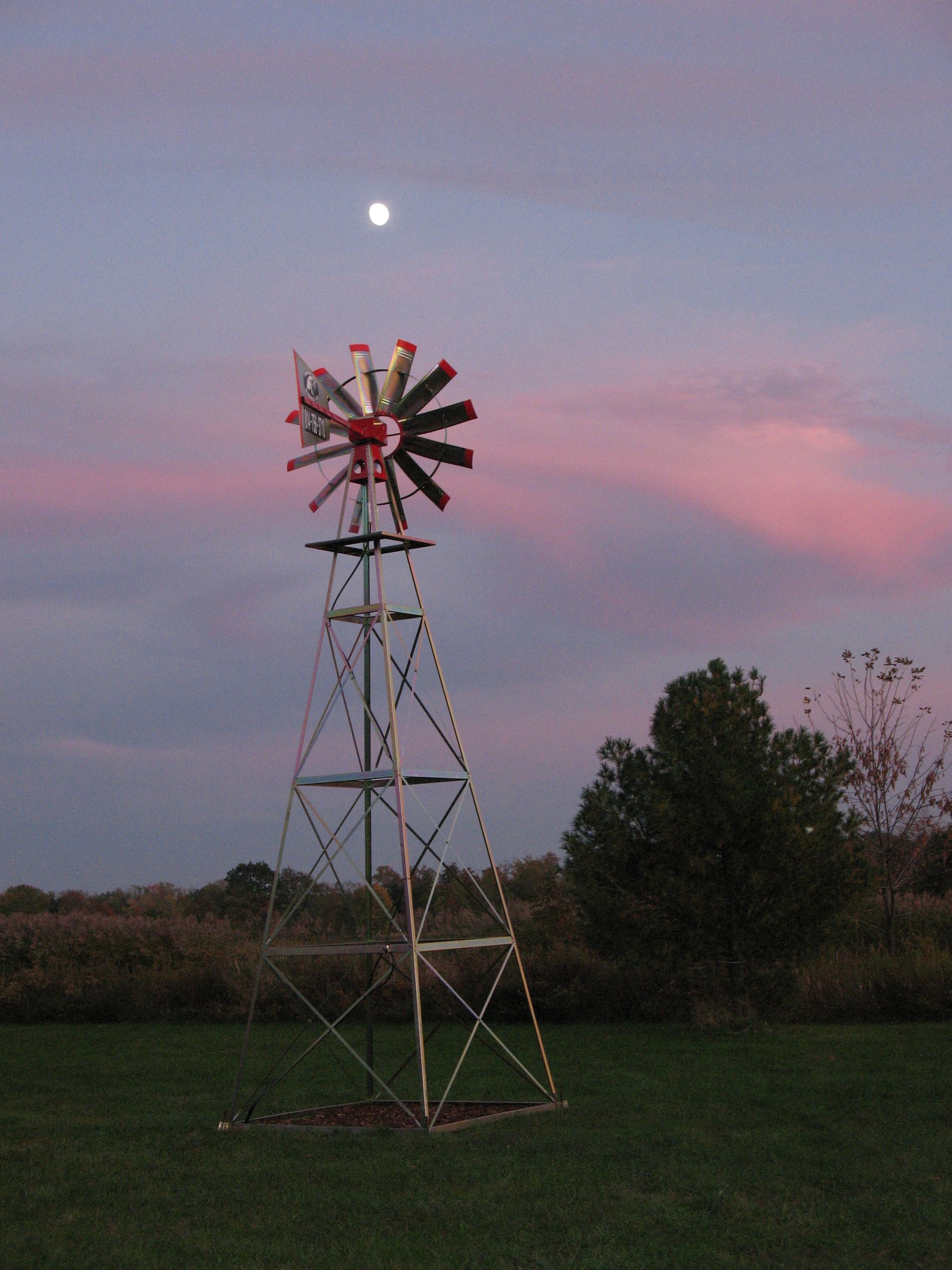 Windmill silhouetted against a dusk sky with moon, blades in red, white and black.