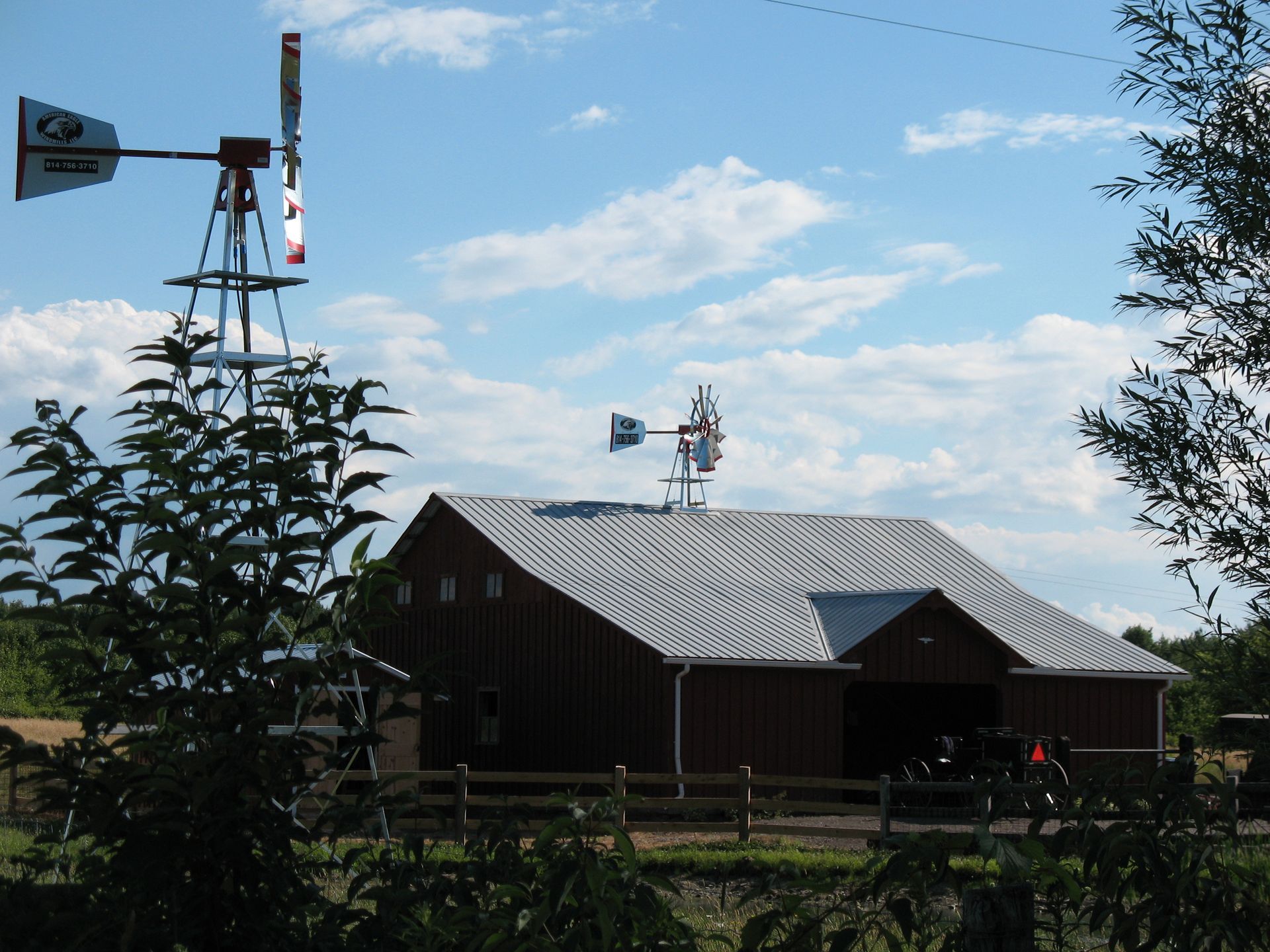 Barn with a red exterior and a silver roof, two windmills, and a cloudy blue sky.