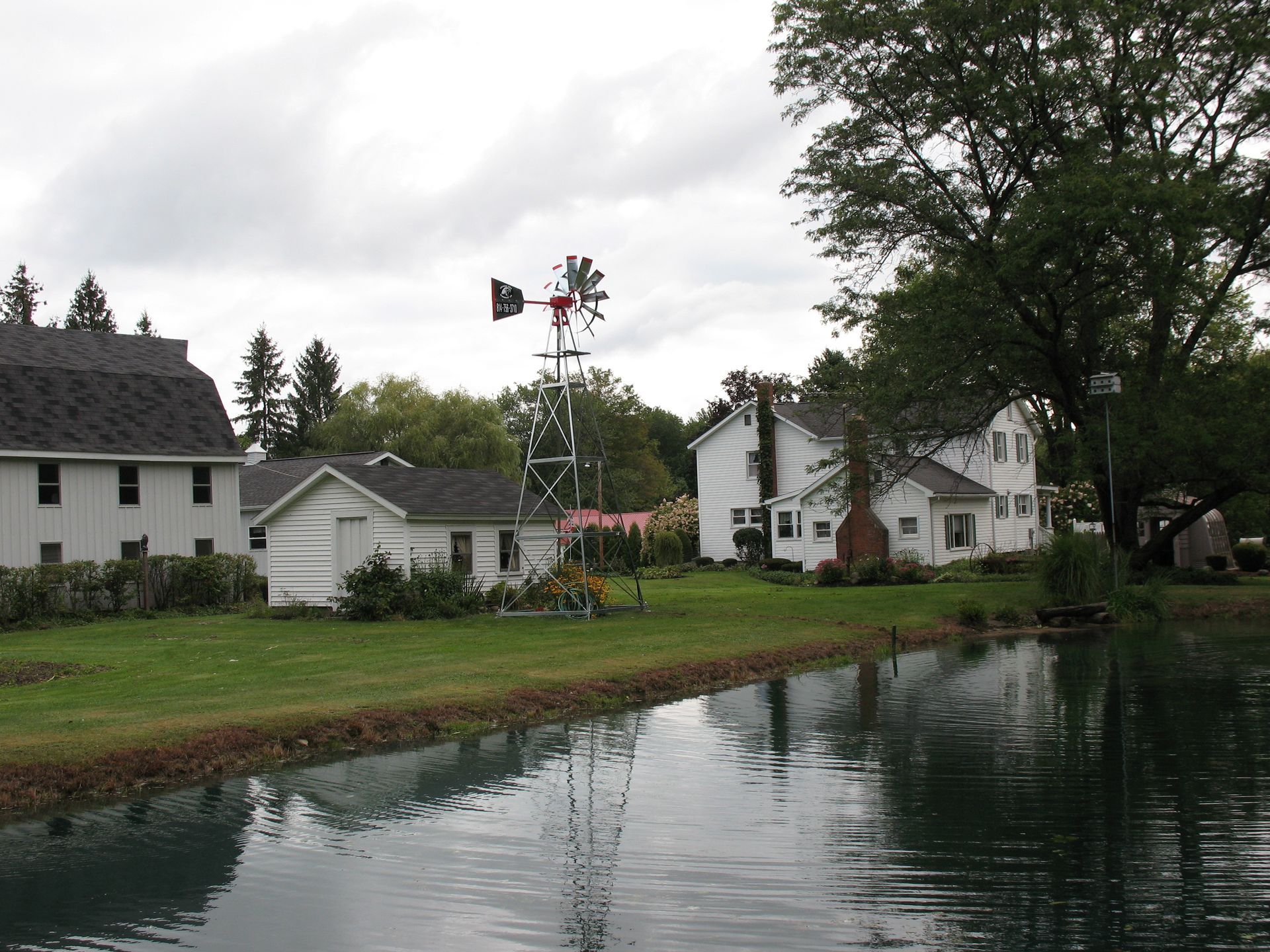 Waterfront rural scene: white houses, windmill, green grass, overcast sky, reflective water.