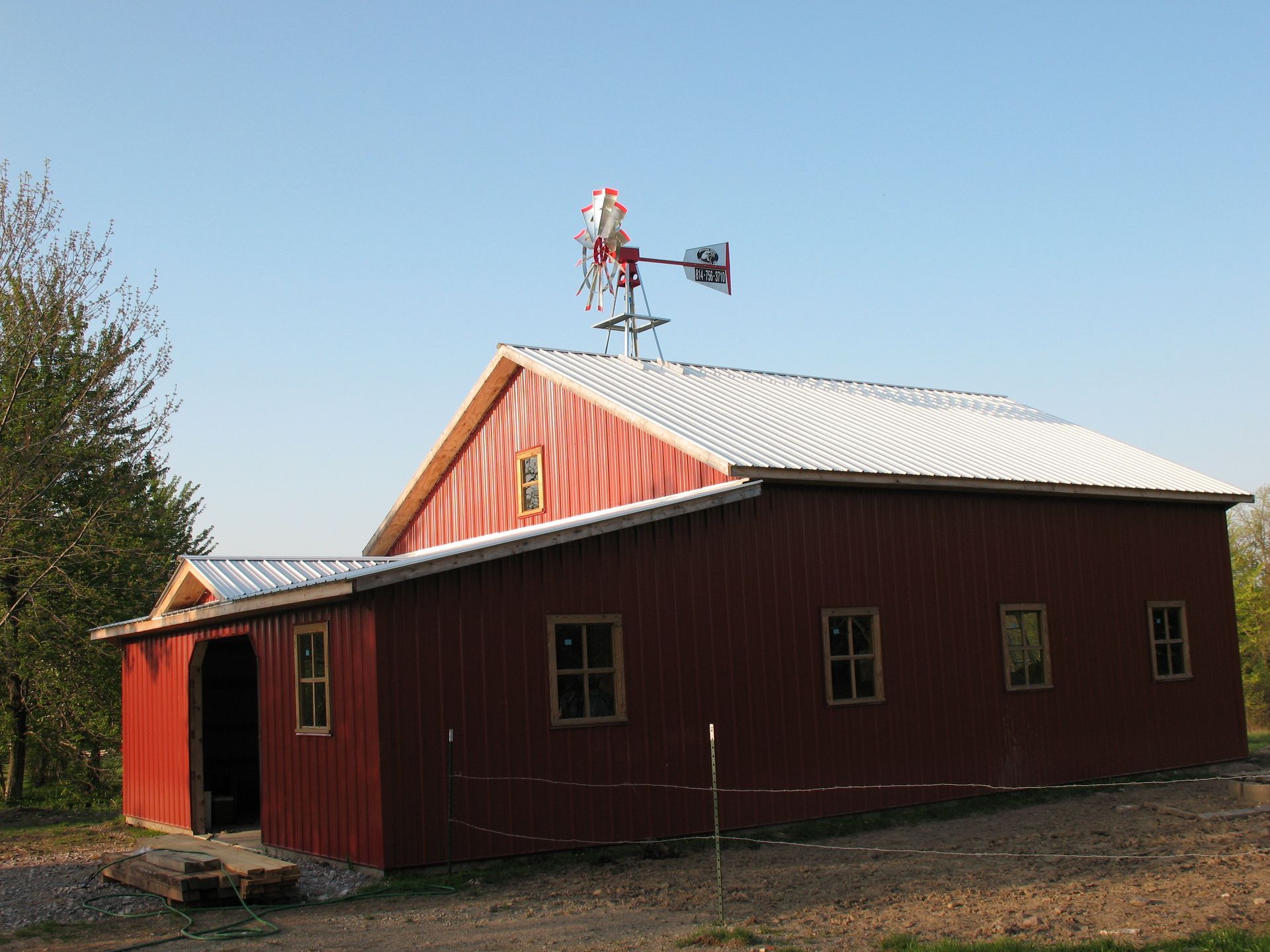 Red barn with white roof and a windmill on top, under a clear blue sky.