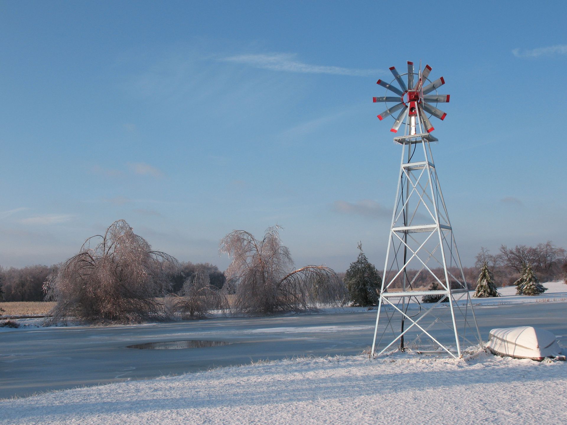 Snowy landscape with windmill, frozen pond, and ice-covered trees under a clear blue sky.