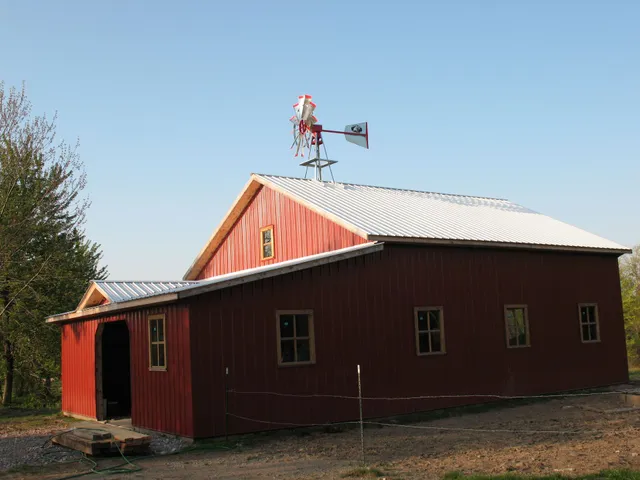 Red barn with white roof and a windmill on top, under a clear blue sky.